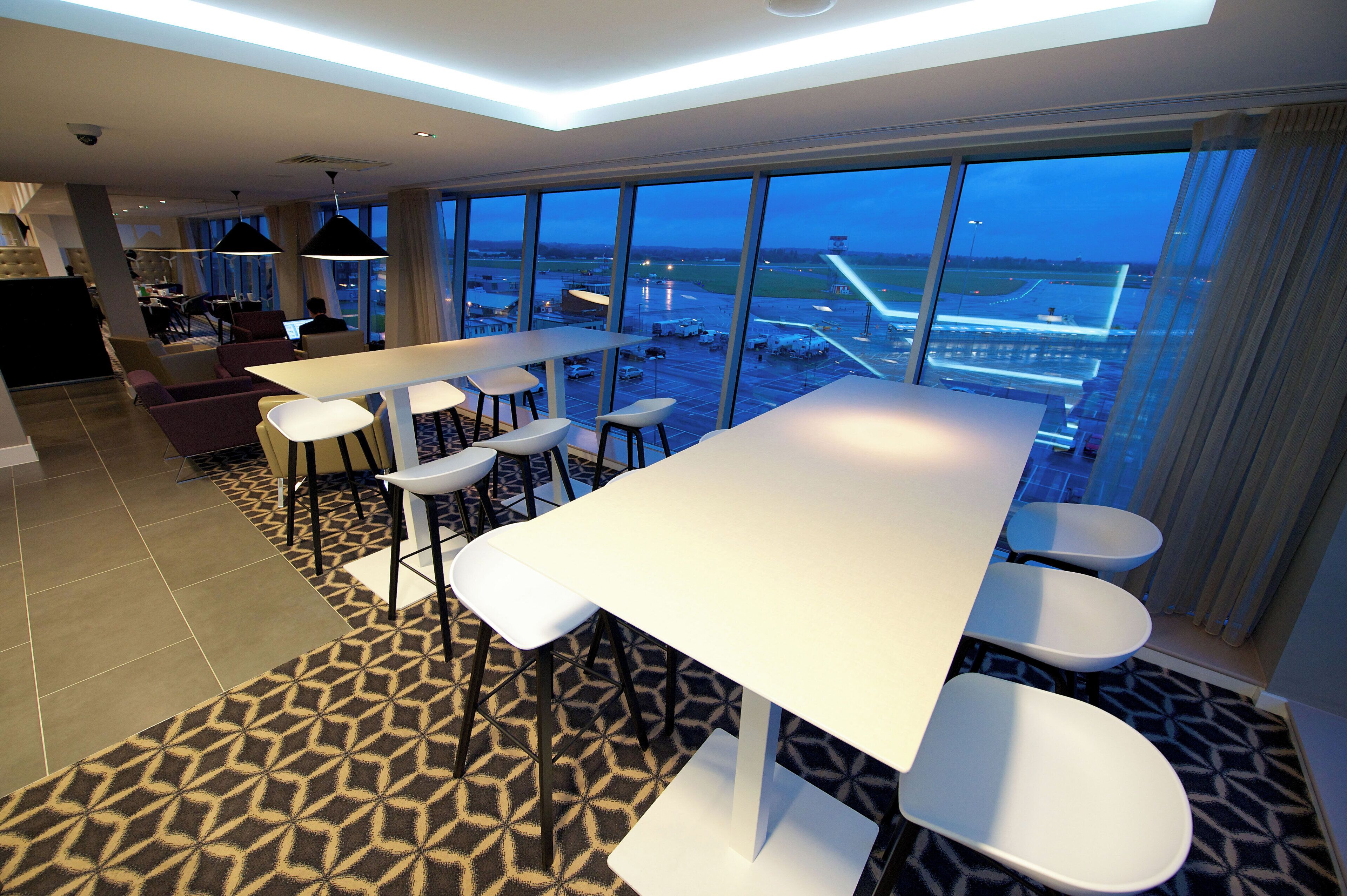 A hotel room with a large window offering a view of an airport. There is a dining area with a table and chairs.