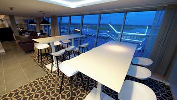 A hotel room with a large window offering a view of an airport. There is a dining area with a table and chairs.