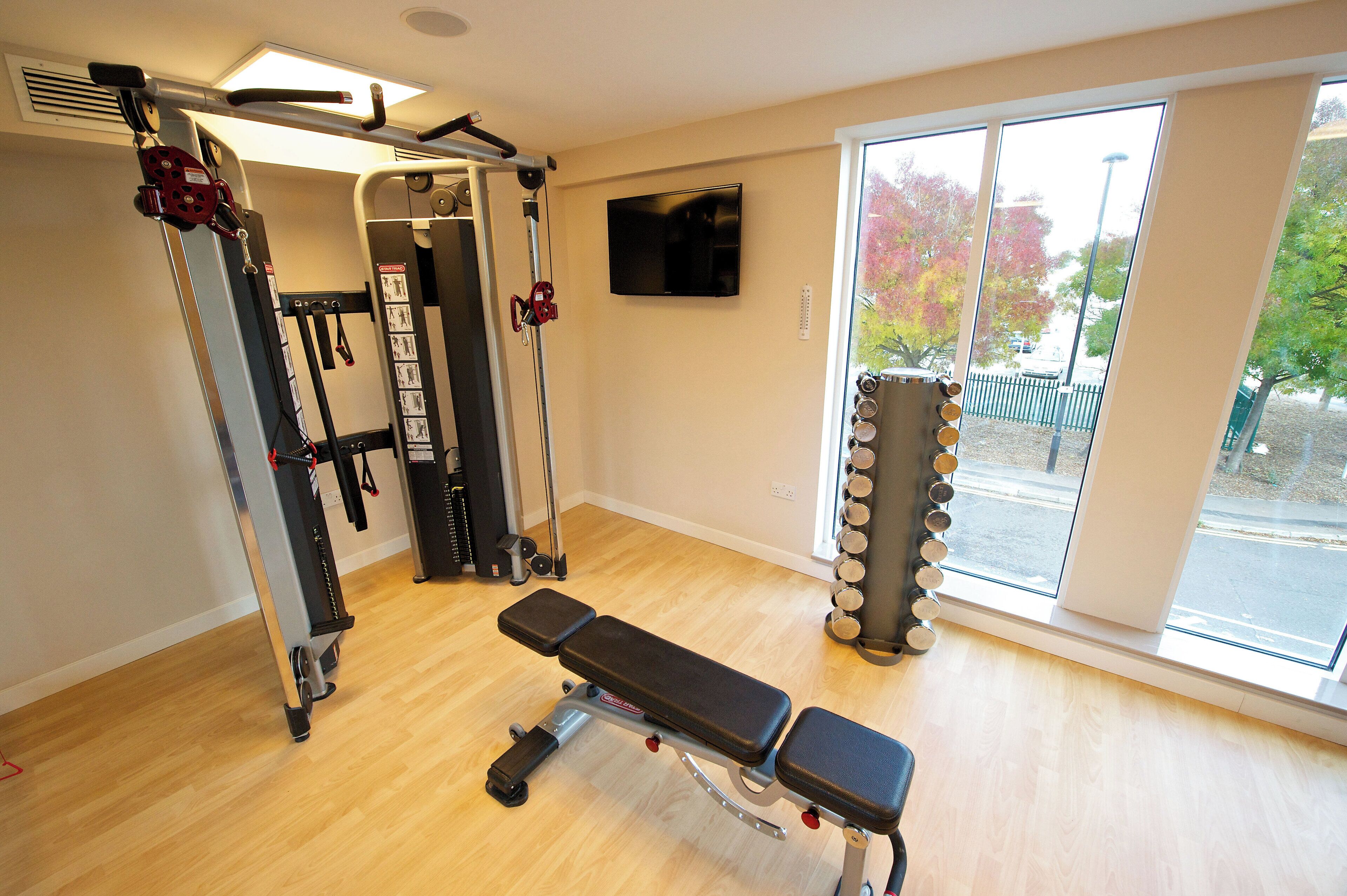 Et fitnesscenter med bænk, træningsmaskiner og et fjernsyn på væggen.