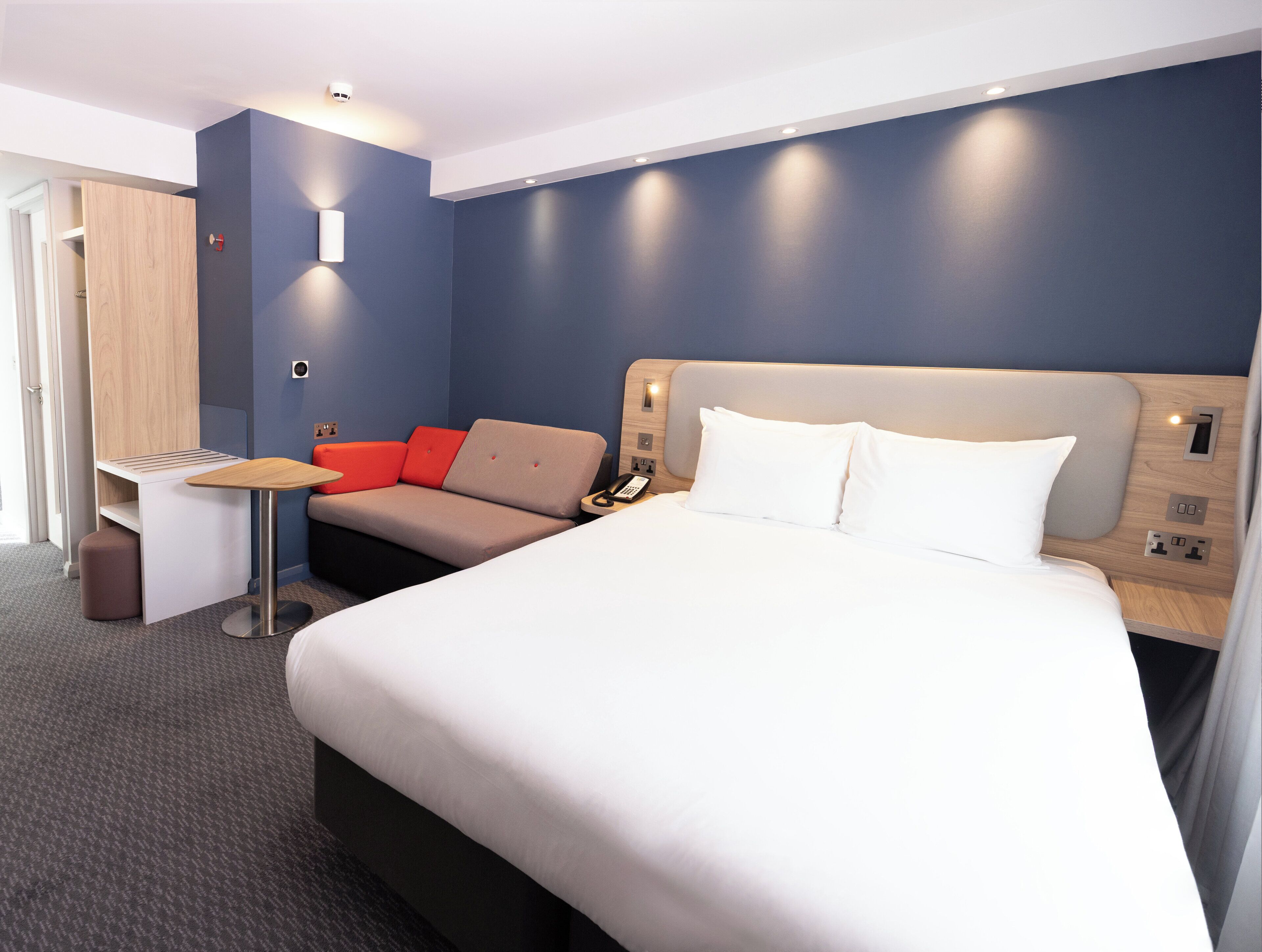 A modern hotel room with a large bed, a desk, and a sofa.