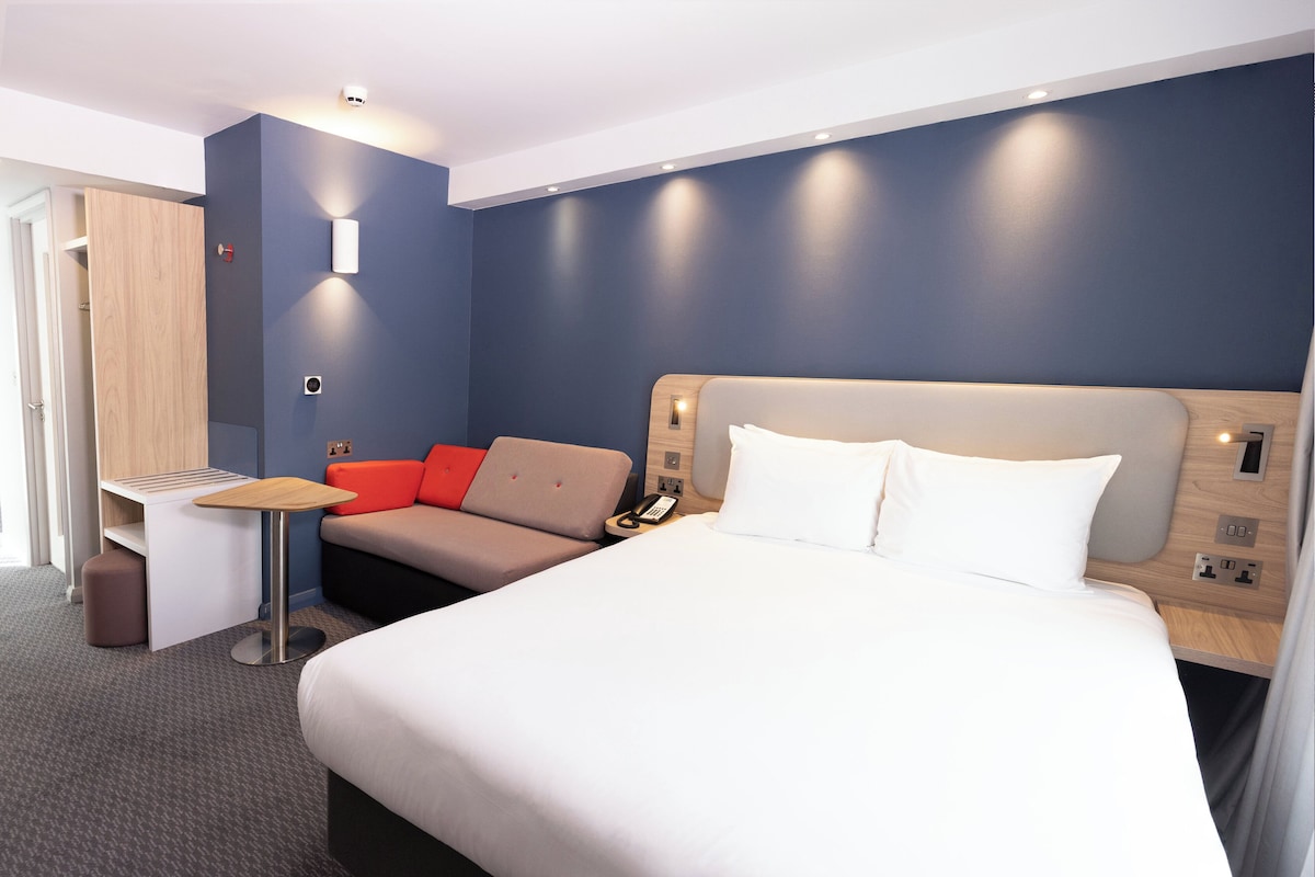 A modern hotel room with a large bed, a desk, and a sofa.