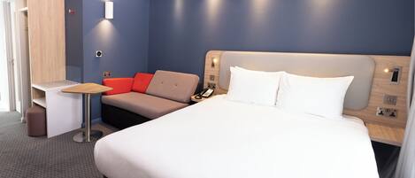 A modern hotel room with a large bed, a desk, and a sofa.