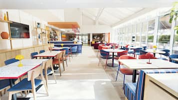 Un comedor amplio e interior con varias mesas y sillas, una zona de bar con estanterías, y grandes ventanales que permiten la entrada de luz natural.