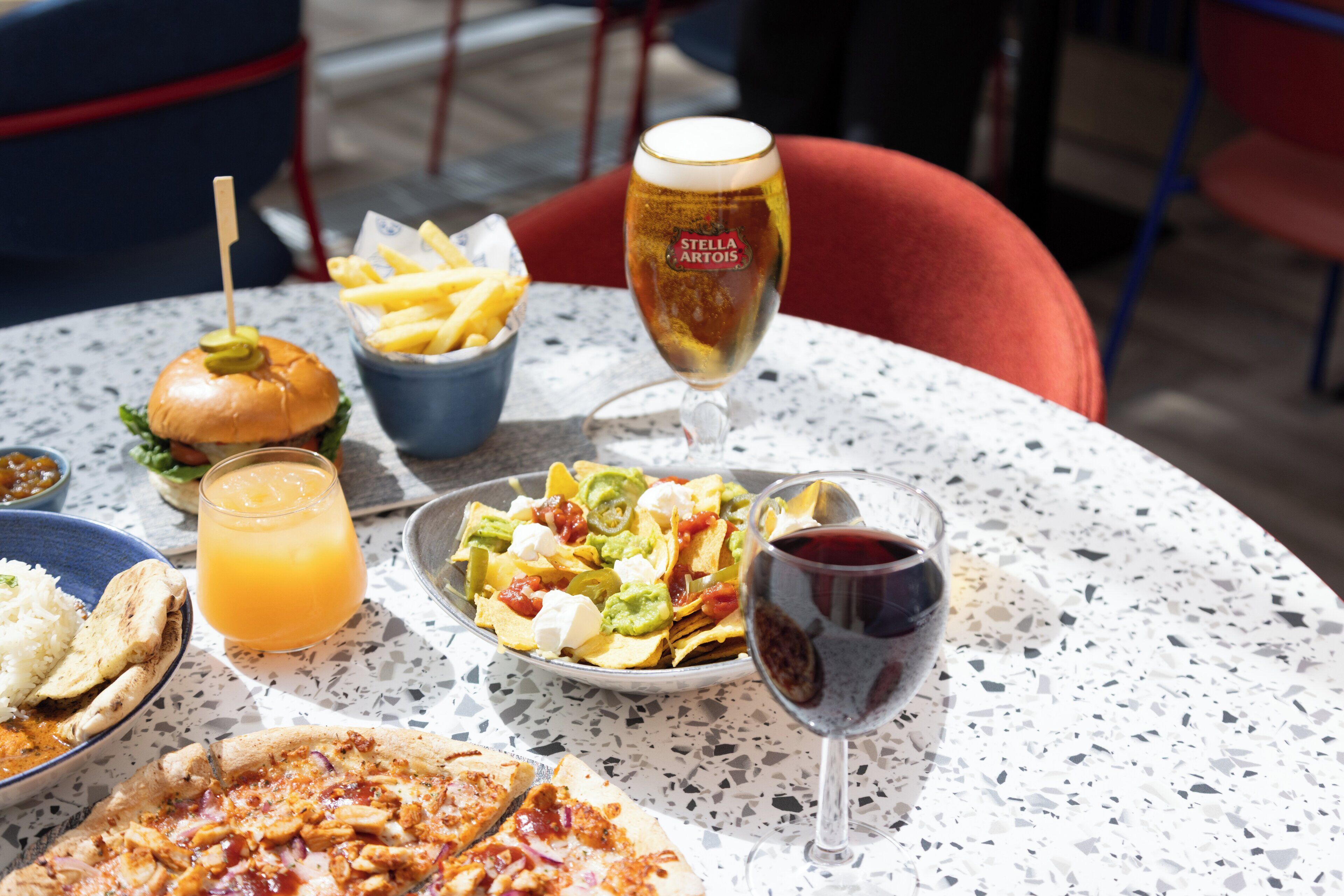 A table with a burger, nachos, pizza, a glass of beer, and a glass of red wine.