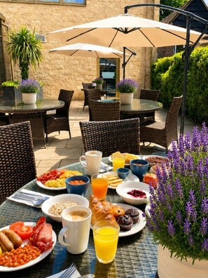 An outdoor dining area with wicker chairs, round tables, and umbrellas.