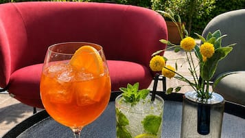 Una mesa con una bebida y un vaso de agua, rodeada de muebles de exterior y sombrillas.