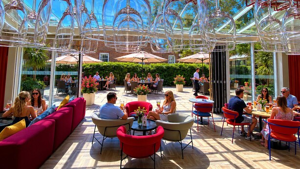 An outdoor dining area with round tables and chairs, surrounded by glass walls and a clear sky. - Holiday Inn Express Windsor by IHG (Windsor)