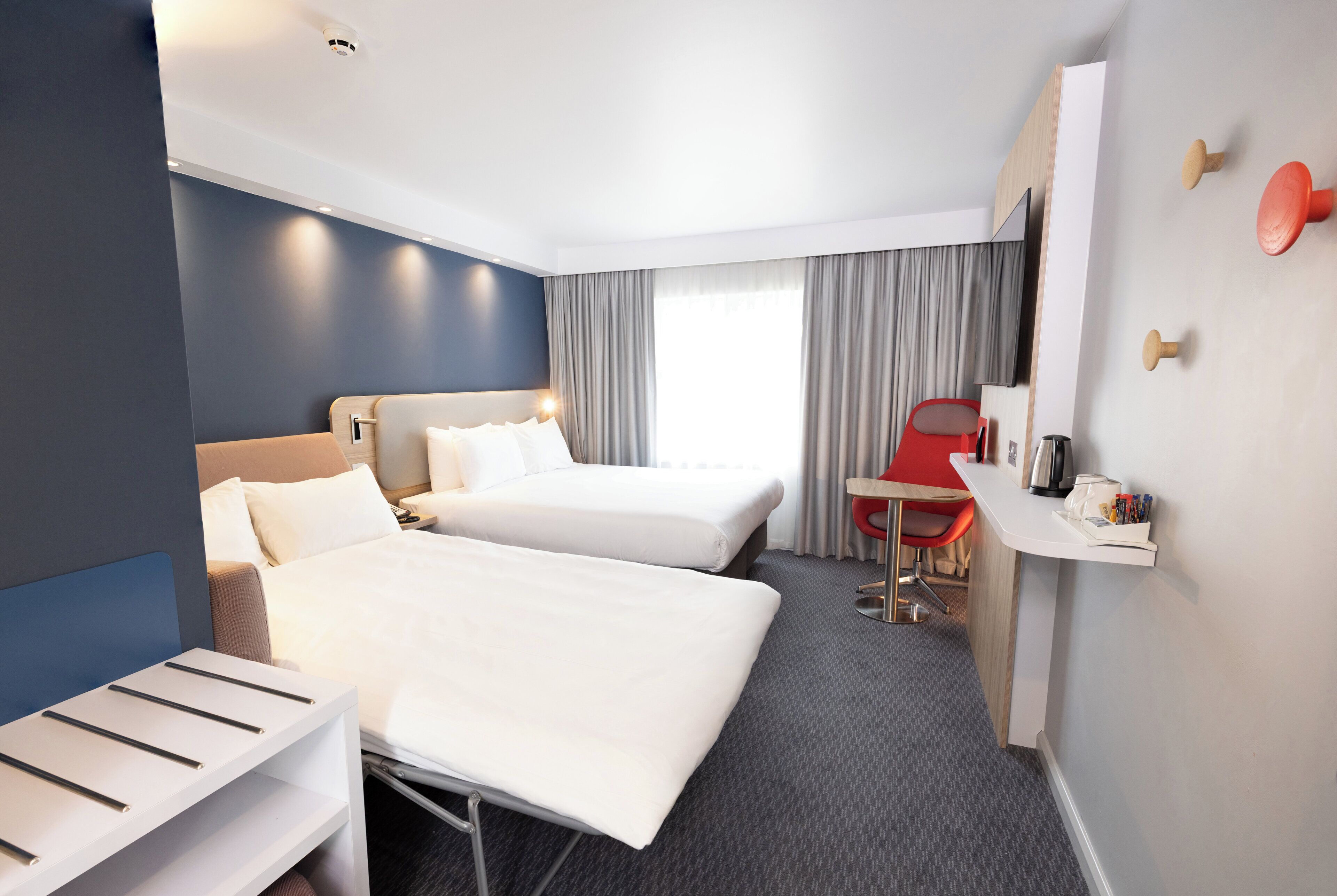 A hotel room with two beds, a desk, a chair, a TV, and a window with curtains.