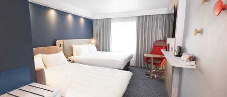 A hotel room with two beds, a desk, a chair, a TV, and a window with curtains.