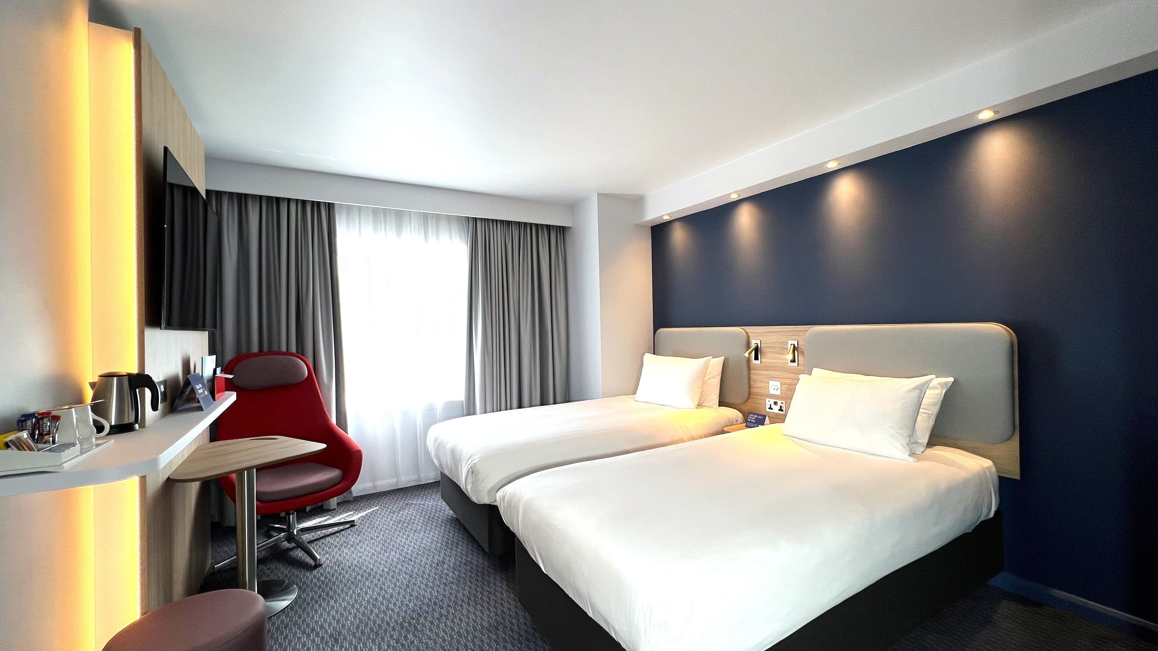 Une chambre d’hôtel avec deux lits, un bureau, une chaise rouge et une vue sur l’extérieur.