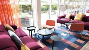 A modern lounge area with purple sofas, orange chairs, and round tables. - Holiday Inn Express Windsor by IHG (Windsor)