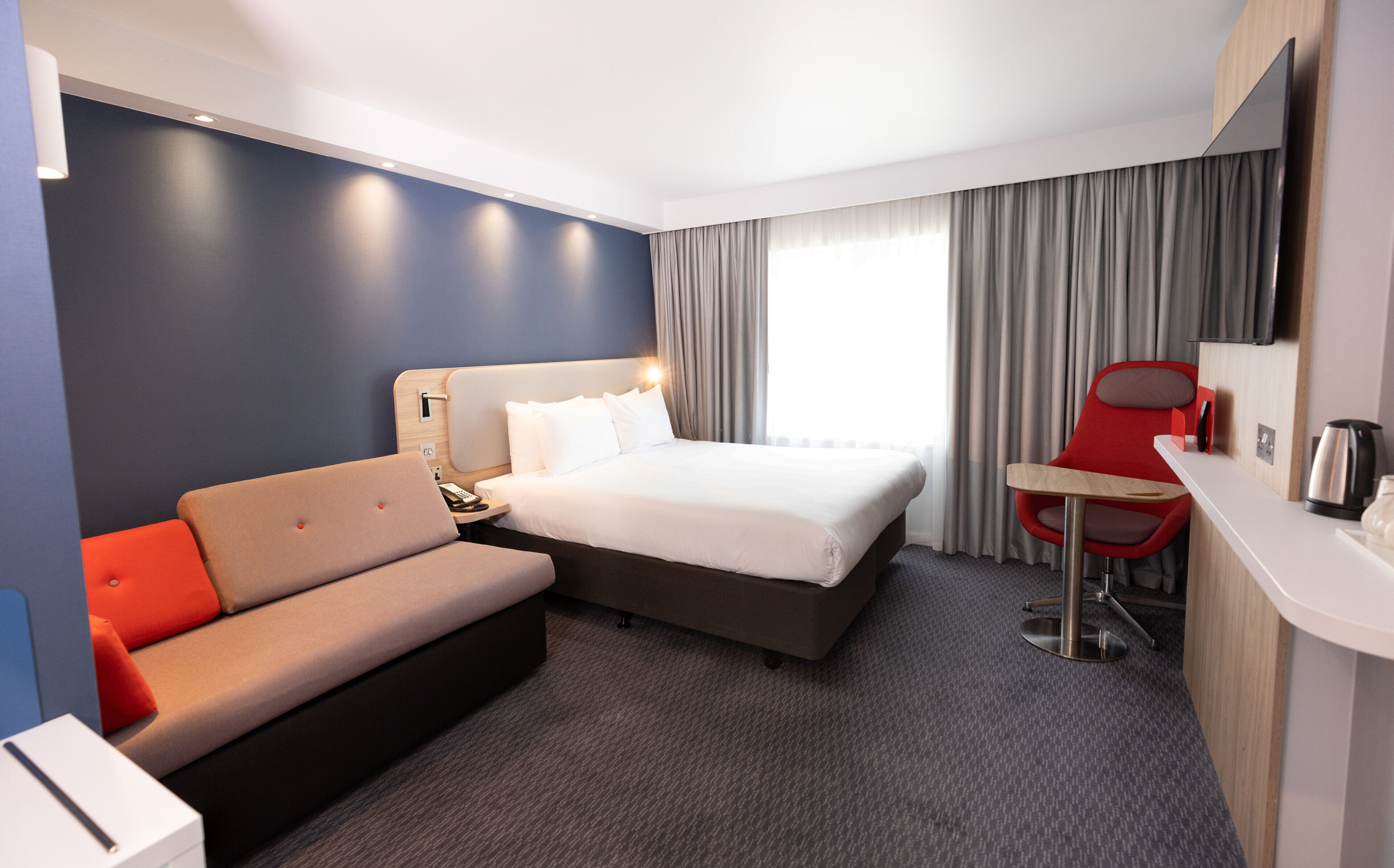 A modern hotel room with a bed, a sofa, a desk, and a chair.
