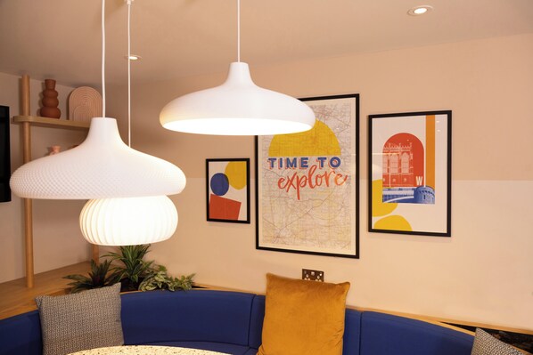 A modern living room with a blue sofa, white pendant lights, and framed artwork on the wall.