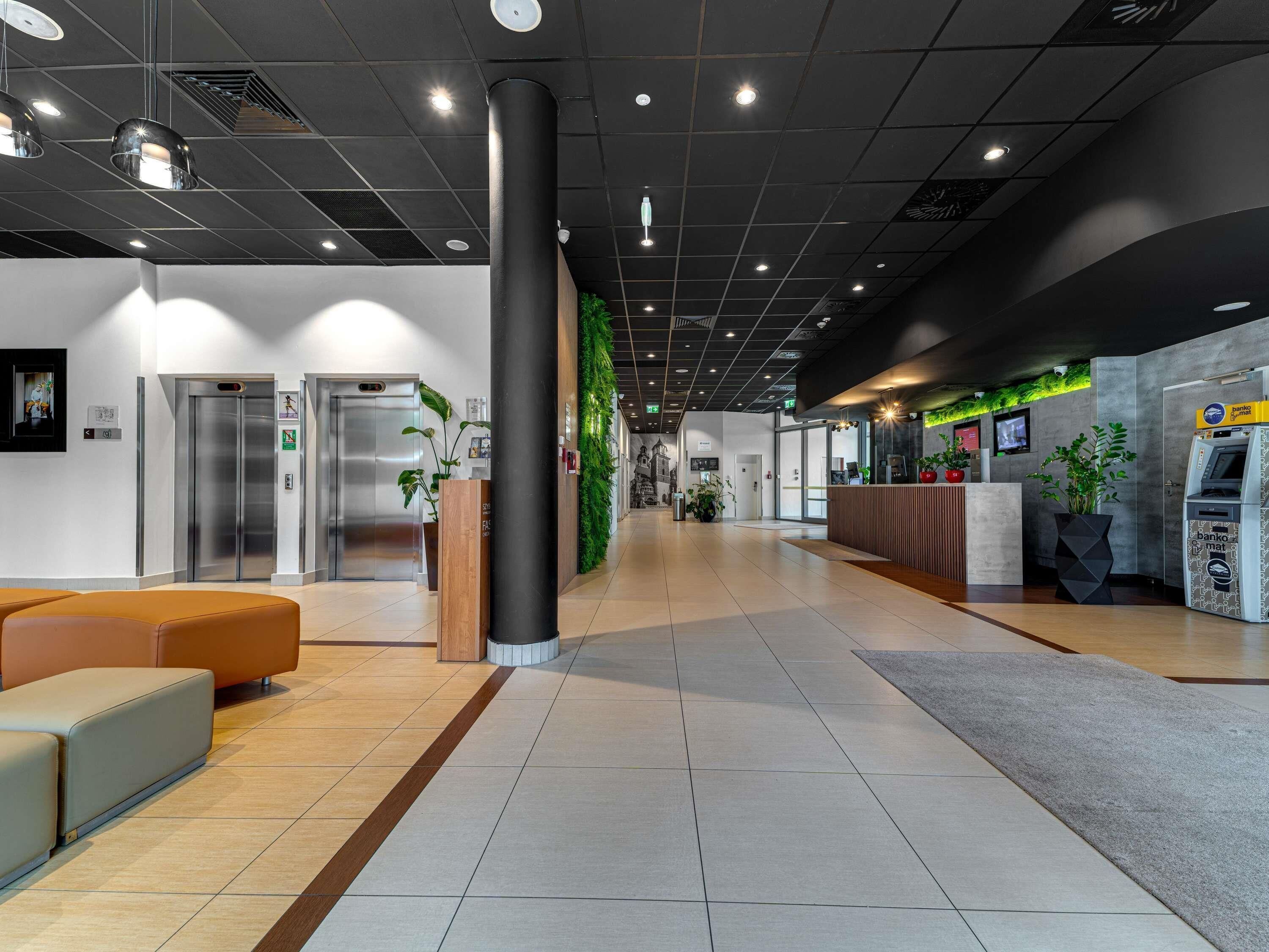 A modern lobby with a reception desk, two elevators, and a seating area.
