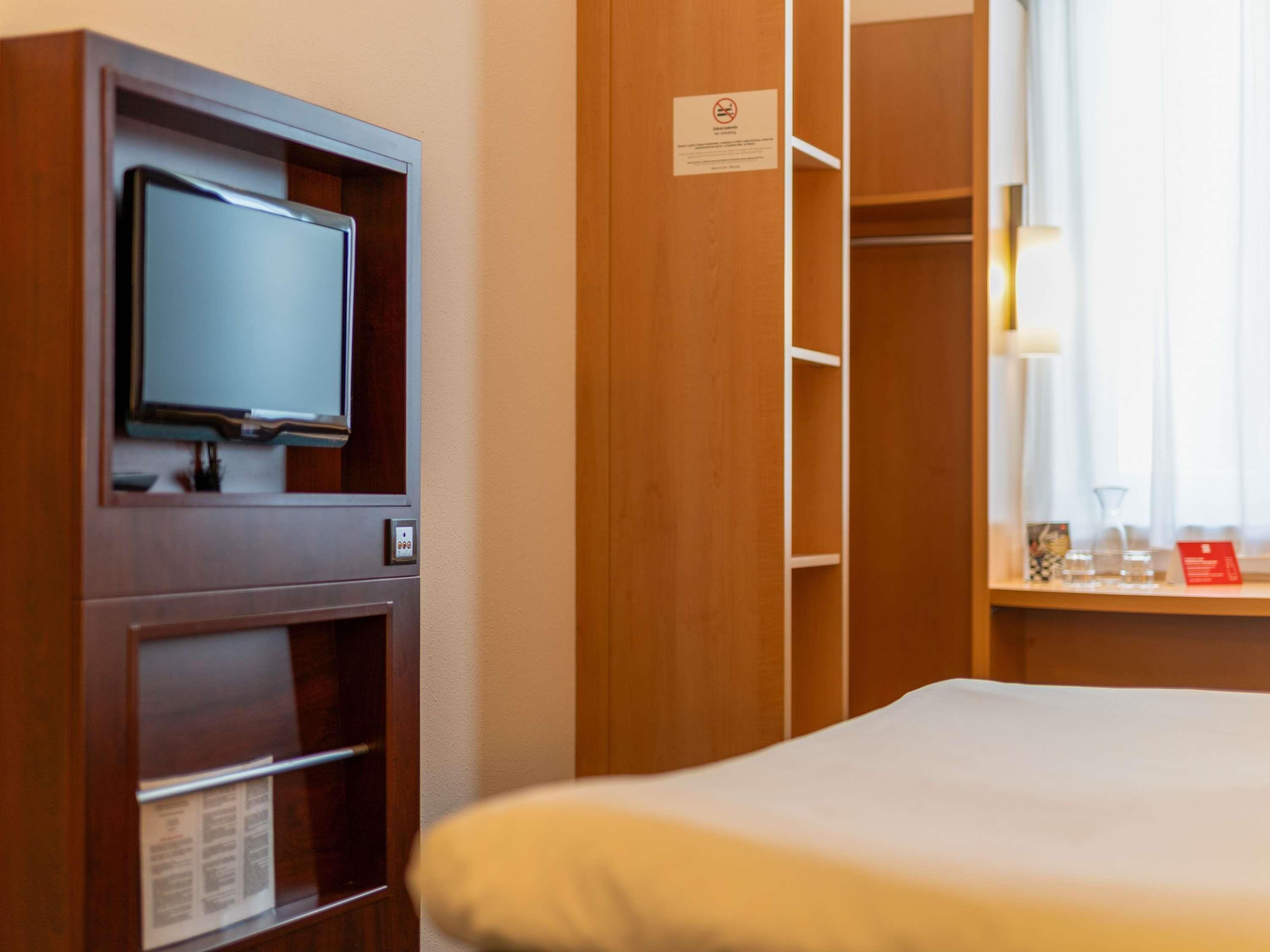 Een hotelkamer met een bed, een televisie bevestigd aan een houten kast en een raam met gordijnen.