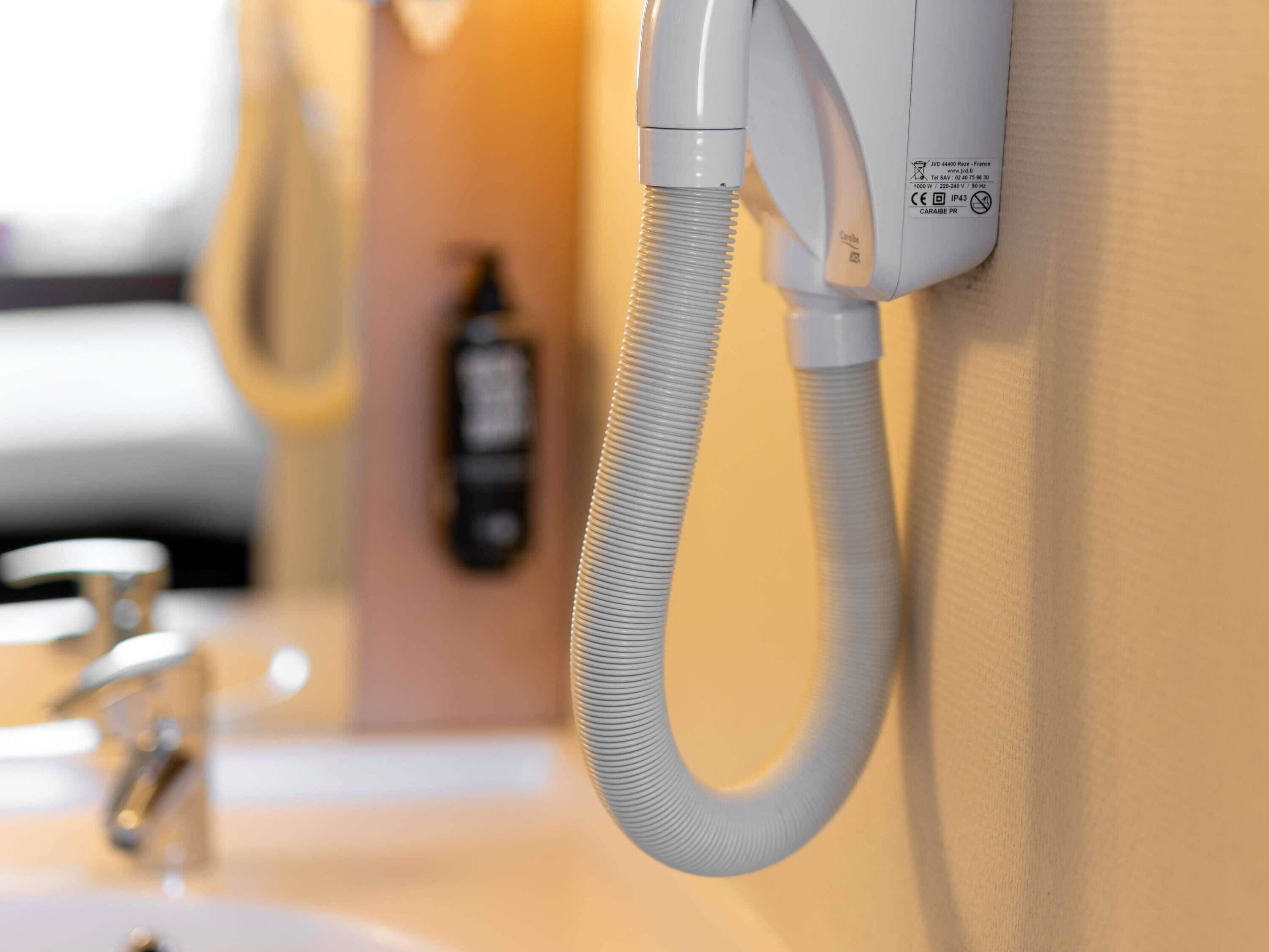 A wall-mounted telephone with a flexible cord, a hand dryer, and a bottle of hand soap in a bathroom.