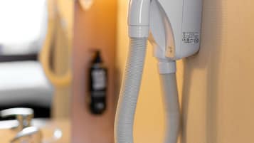 A wall-mounted telephone with a flexible cord, a hand dryer, and a bottle of hand soap in a bathroom.