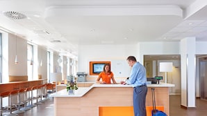 A hotel reception area with a modern design, featuring a reception desk, a digital screen, and a seating area with bar stools. - ibis Krakow Stare Miasto (Kraków)