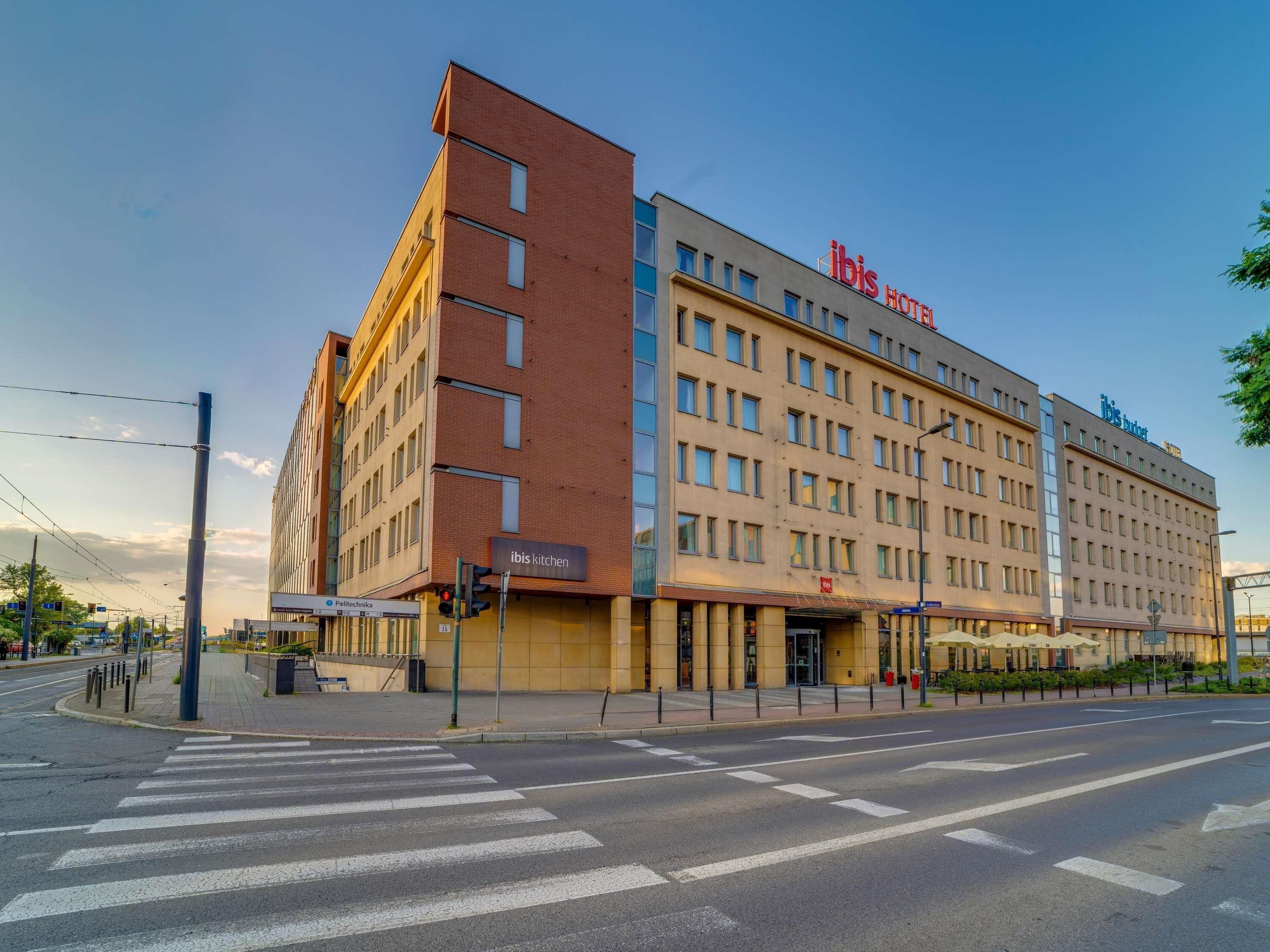 Un hotel de varios pisos con un llamativo letrero de 'ibis Hotel', una entrada visible y un paso de peatones.