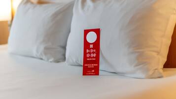 A hotel room with a neatly made bed, white pillows, and a red tag on the bed.