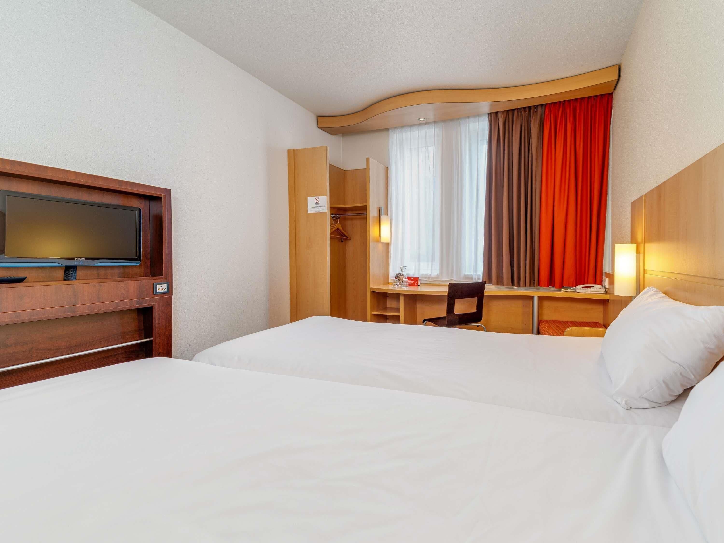 Une chambre d’hôtel avec deux lits, un bureau, une télévision et une fenêtre avec des rideaux.