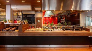 A buffet setup with various food items, a chalkboard menu, and a kitchen area with stainless steel appliances. - ibis Krakow Stare Miasto (Kraków)