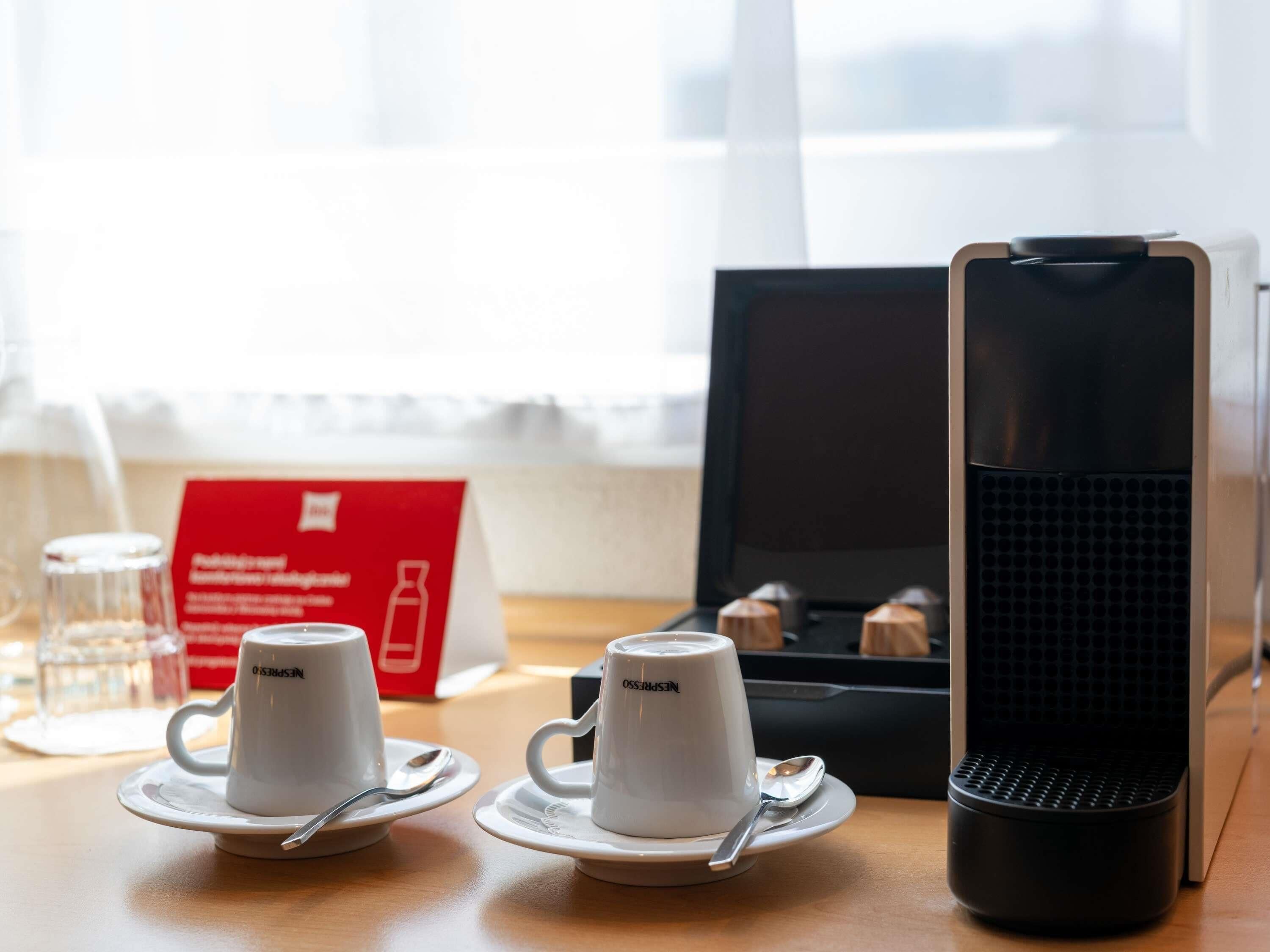 Two white cups with saucers and a spoon on a wooden table, a black speaker, and a red sign in the background.