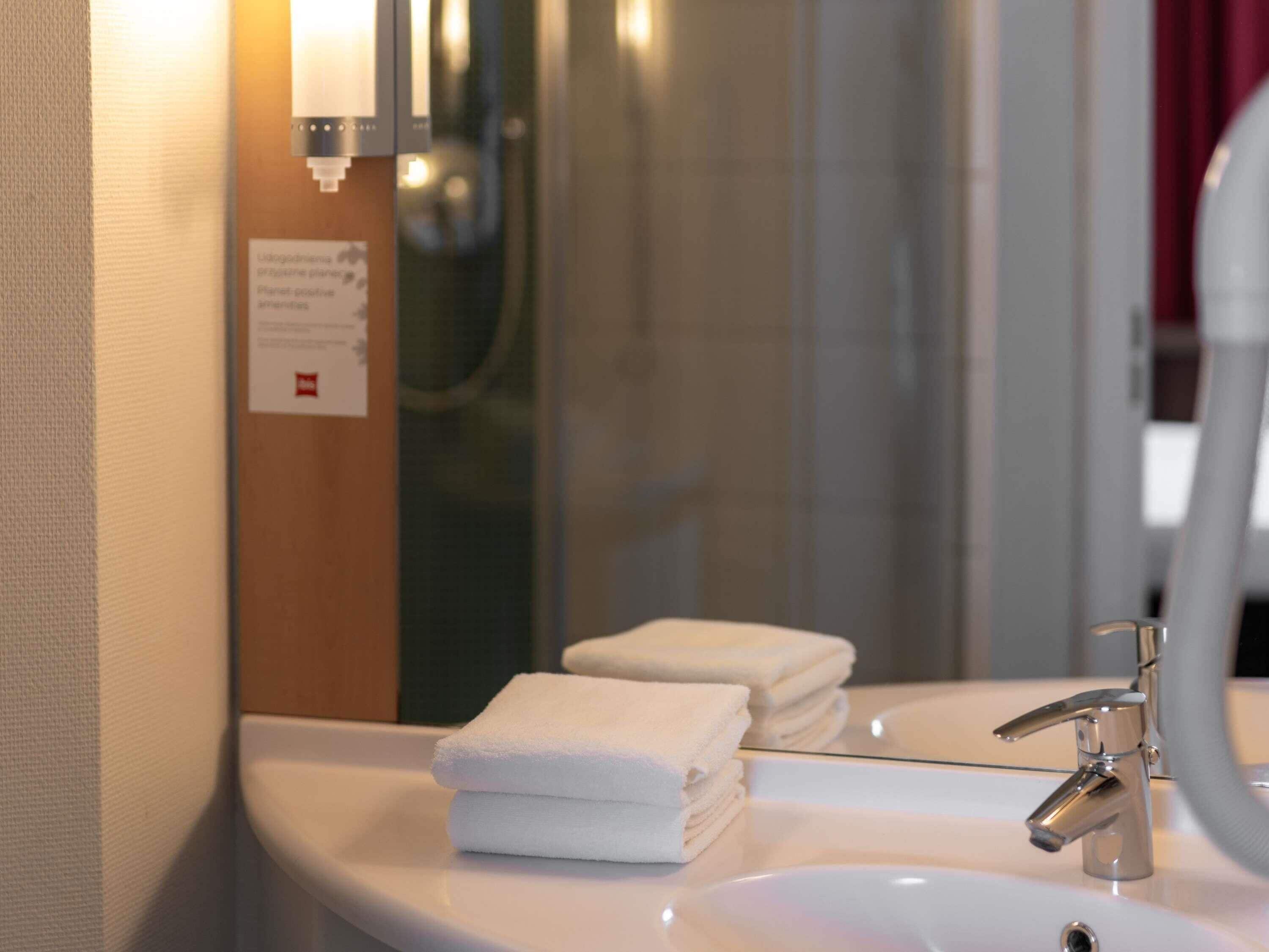 A bathroom with a sink, a mirror, and a towel stack.