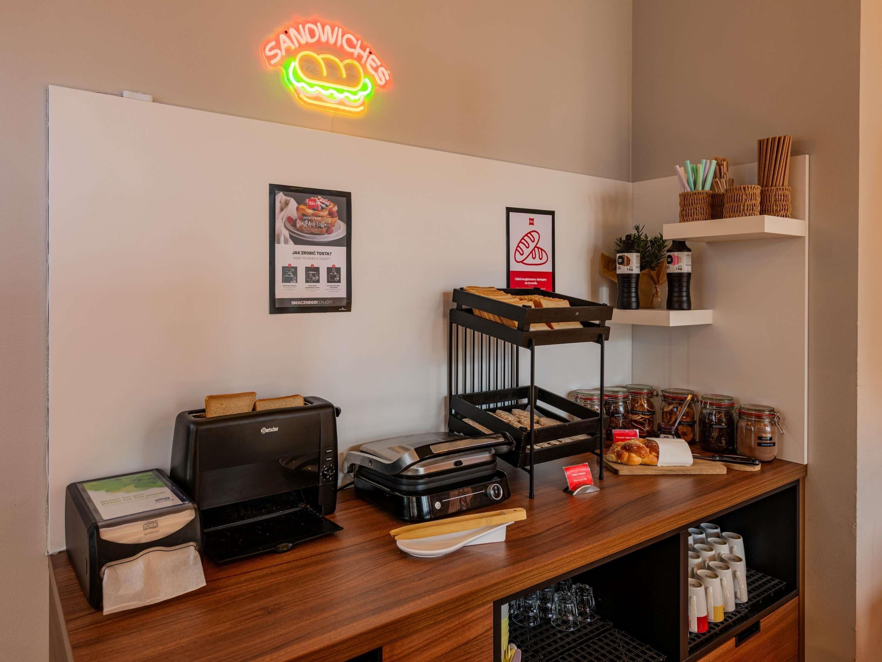 A sandwich station with a neon sign, a toaster, a coffee machine, and various condiments.