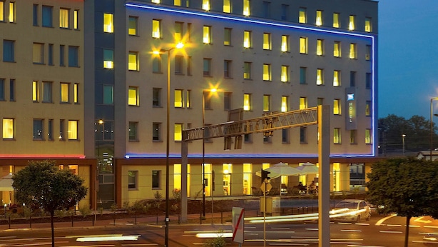 A multi-story hotel with illuminated signage, a covered outdoor seating area, and a street view with traffic lights. - ibis Krakow Stare Miasto (Kraków)