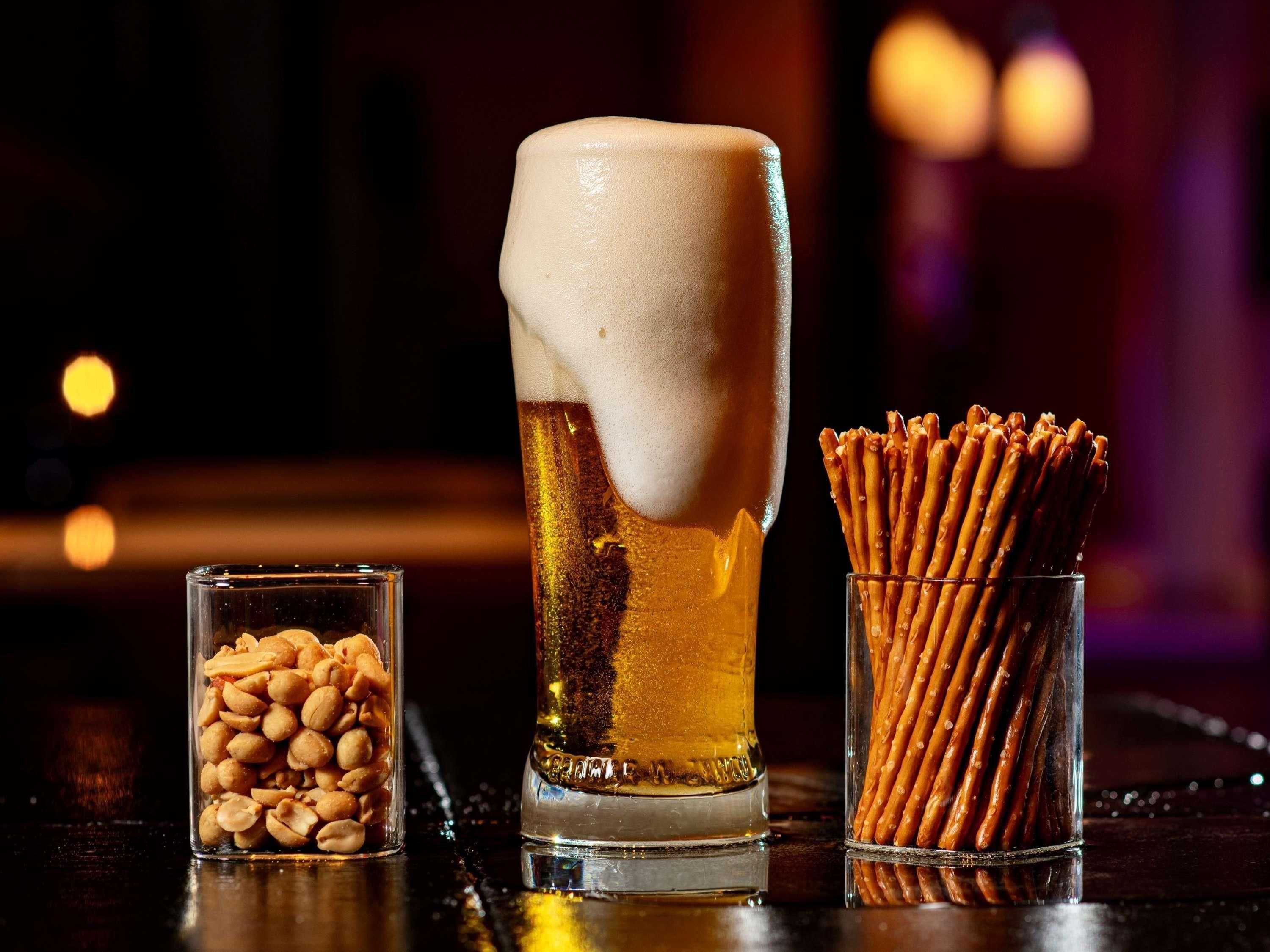 Ein hohes Glas Bier mit Schaum, ein kleines Glas Erdnüsse und ein Glas Brezeln.