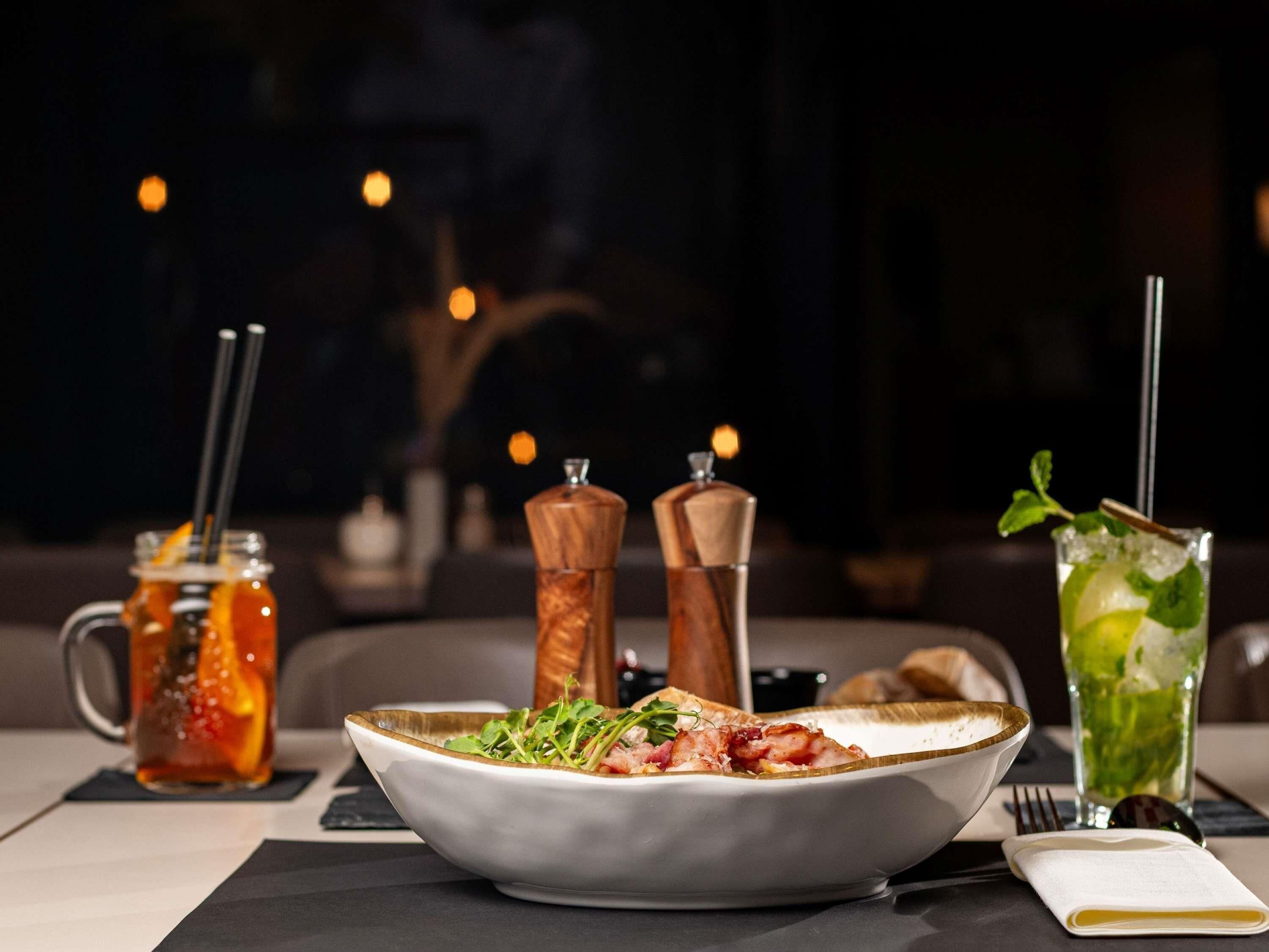 A dining table with a plate of food, a drink, and a candle.