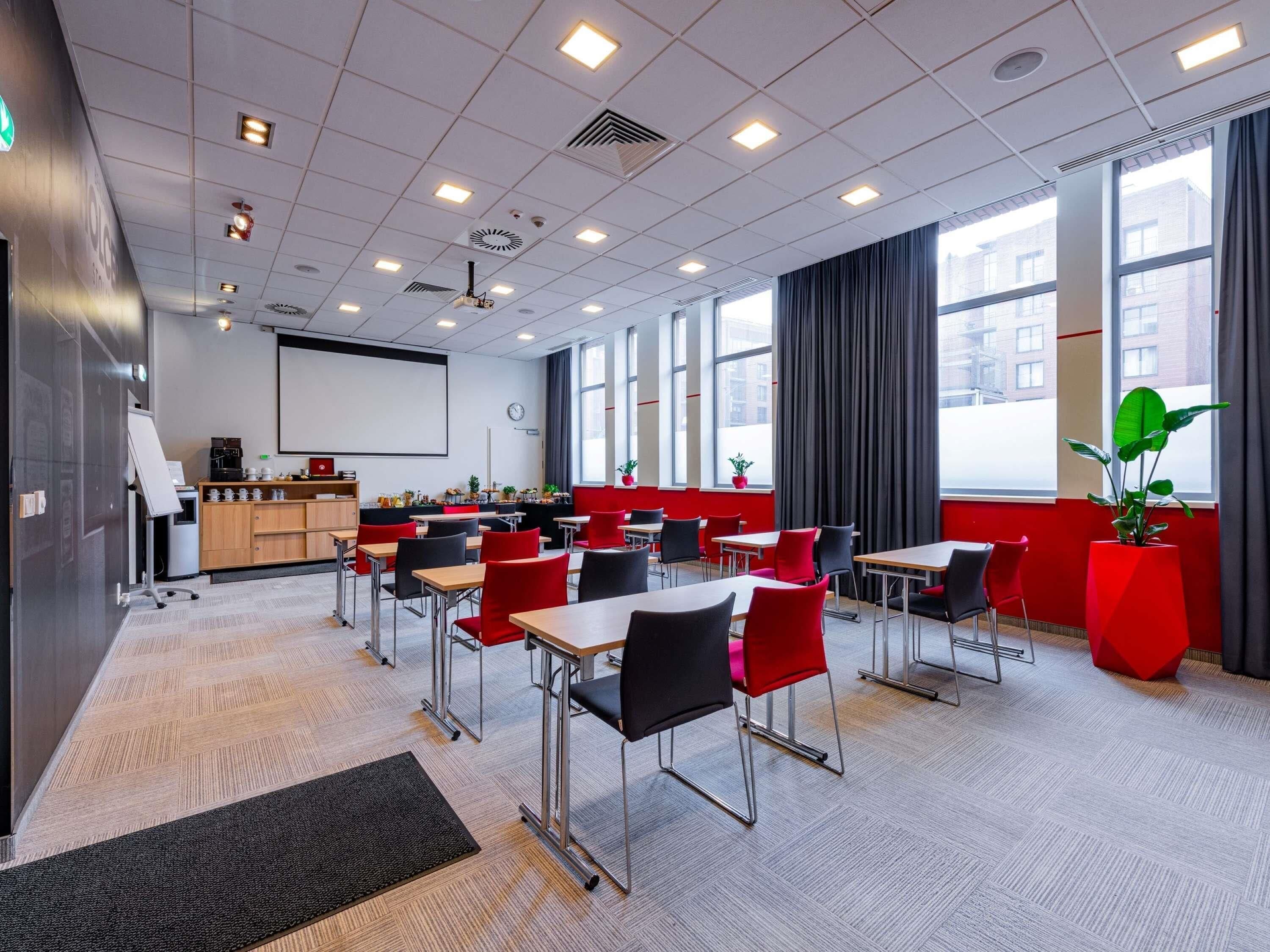 Een moderne vergaderzaal met tafels, stoelen, een projectiescherm en grote ramen.