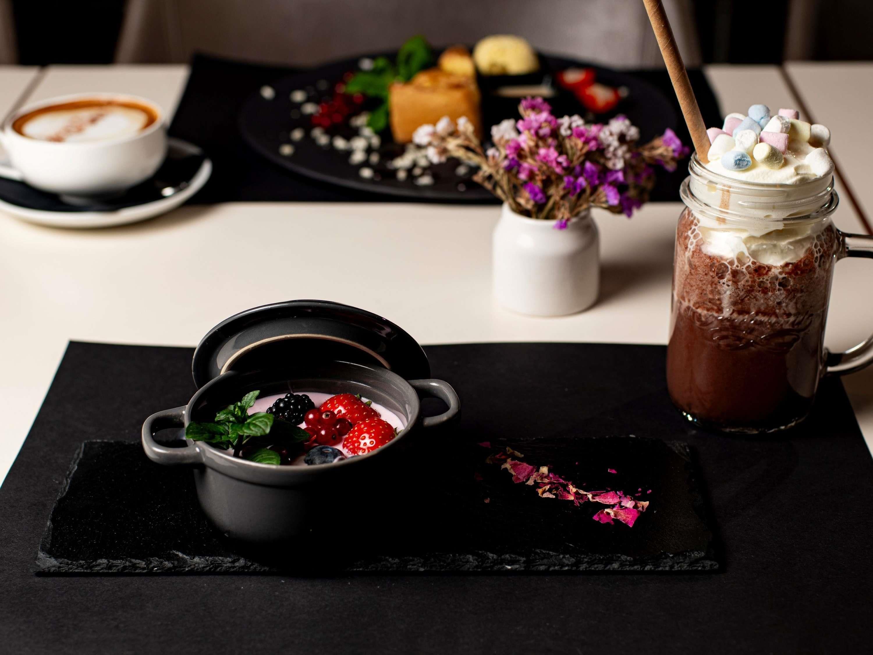 A dessert setting with a bowl of berries, a chocolate drink, and a plate with pastries.