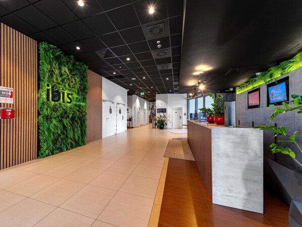 Un moderno vestíbulo de hotel con mostrador de recepción, una pared verde con helechos y un panel de madera.