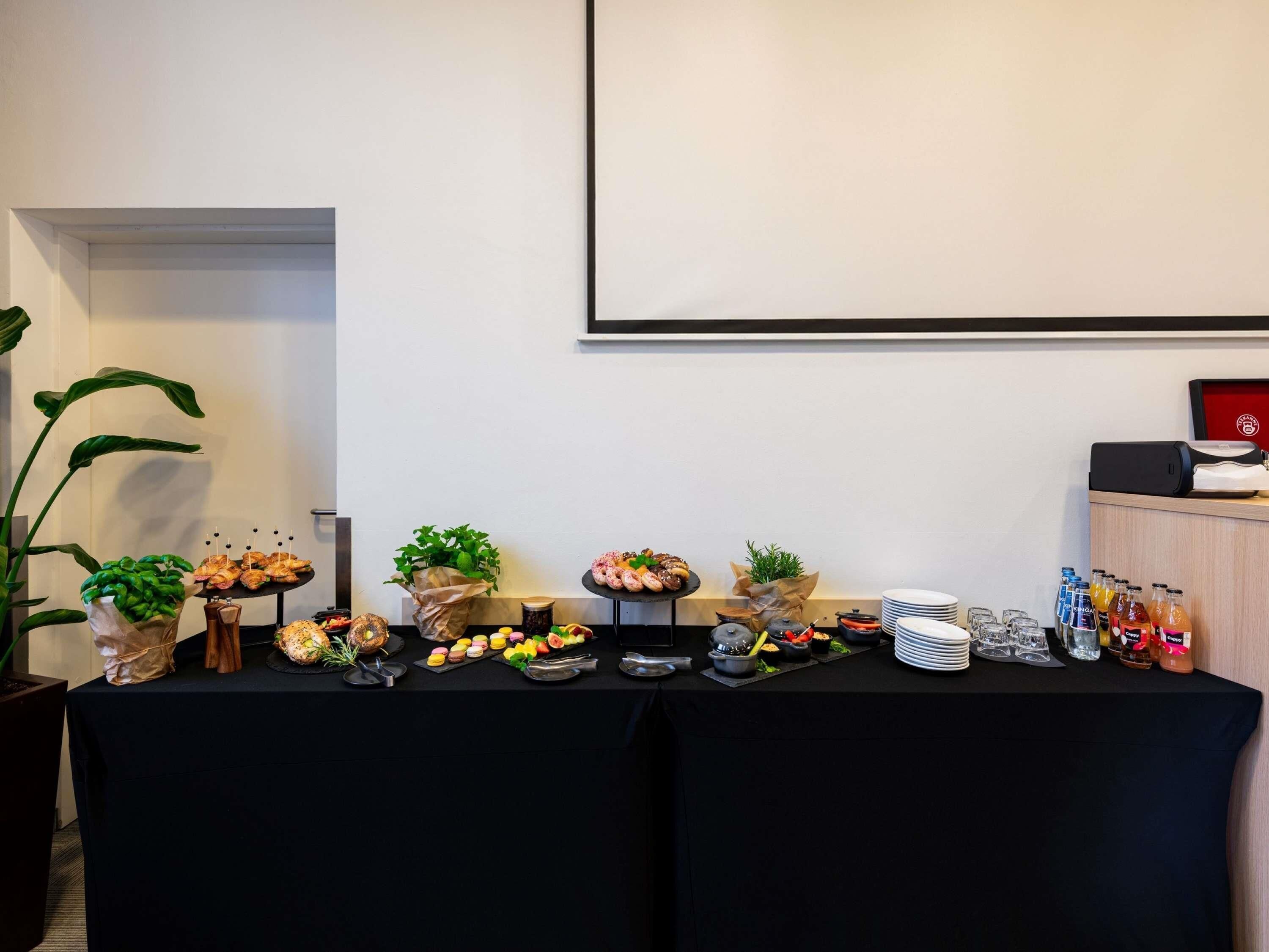 A buffet table with various food items and beverages, a projector screen, and a plant on the left.