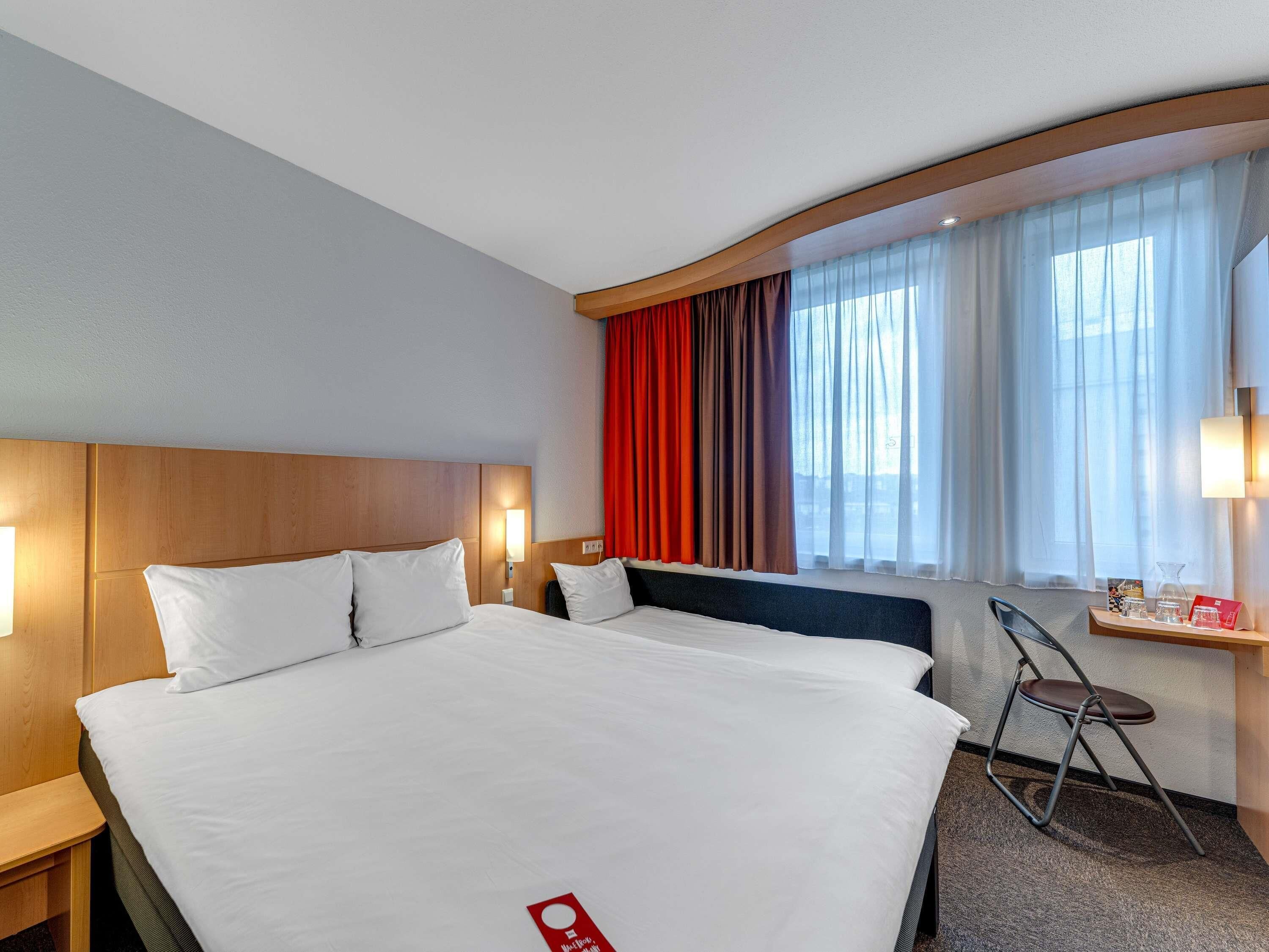 A hotel room with a large bed, a desk with a chair, and a window with curtains.