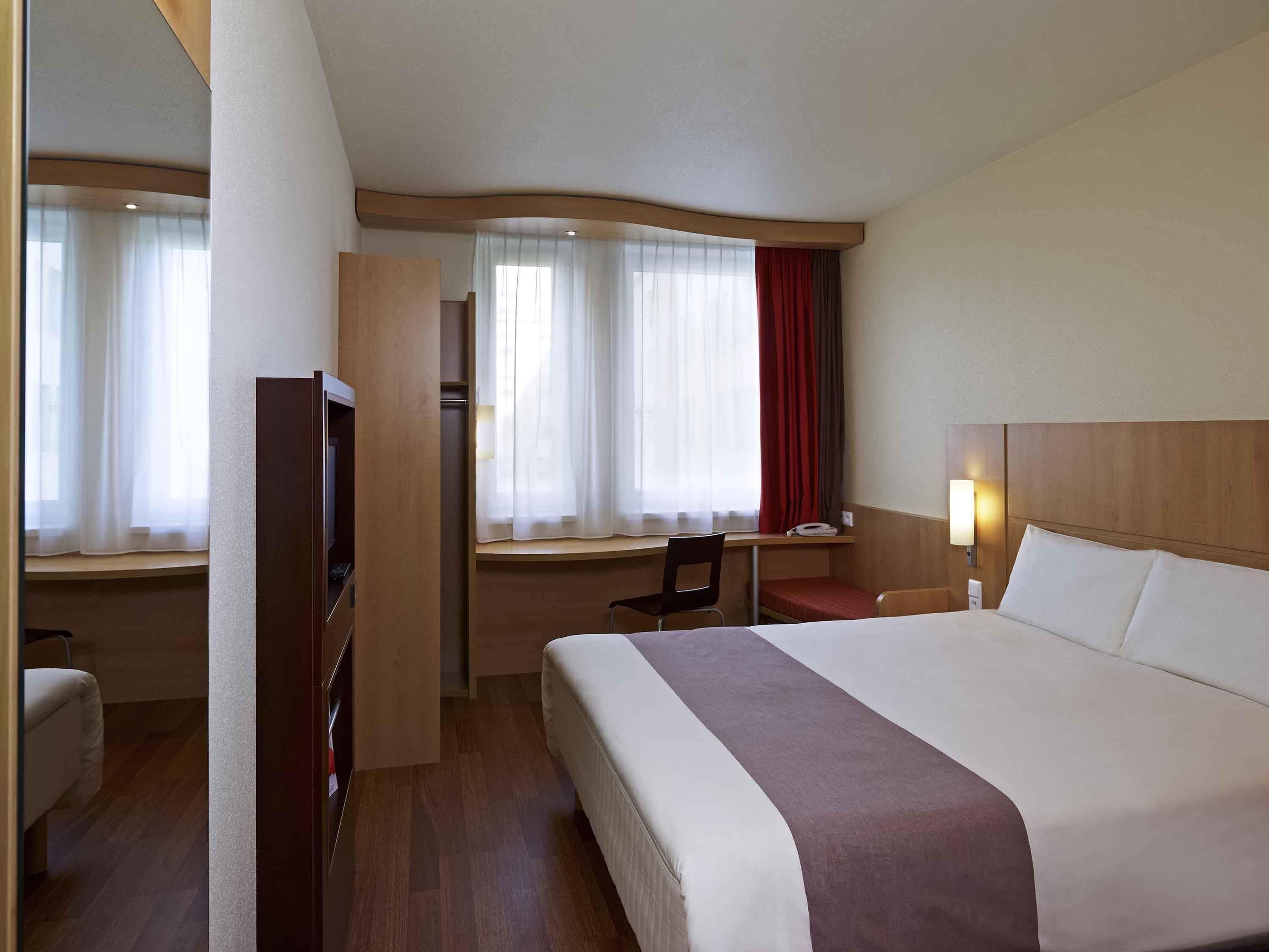 Une chambre d’hôtel équipée d’un lit, d’un bureau, d’une chaise, d’une télévision et d’une fenêtre avec des rideaux.