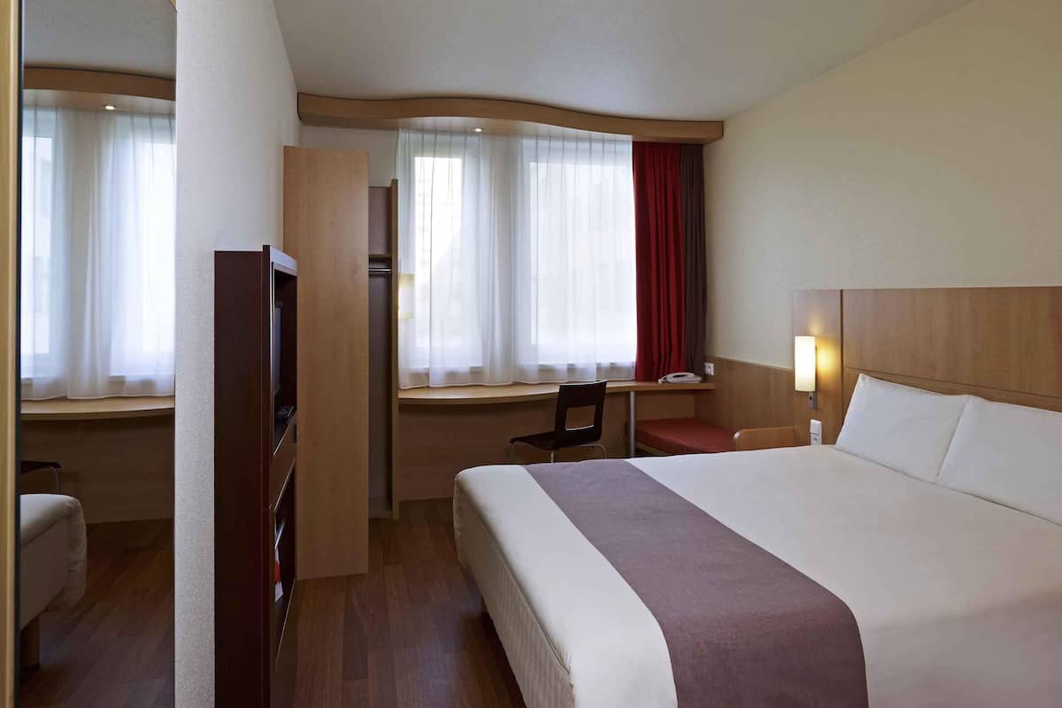 Une chambre d’hôtel équipée d’un lit, d’un bureau, d’une chaise, d’une télévision et d’une fenêtre avec des rideaux.