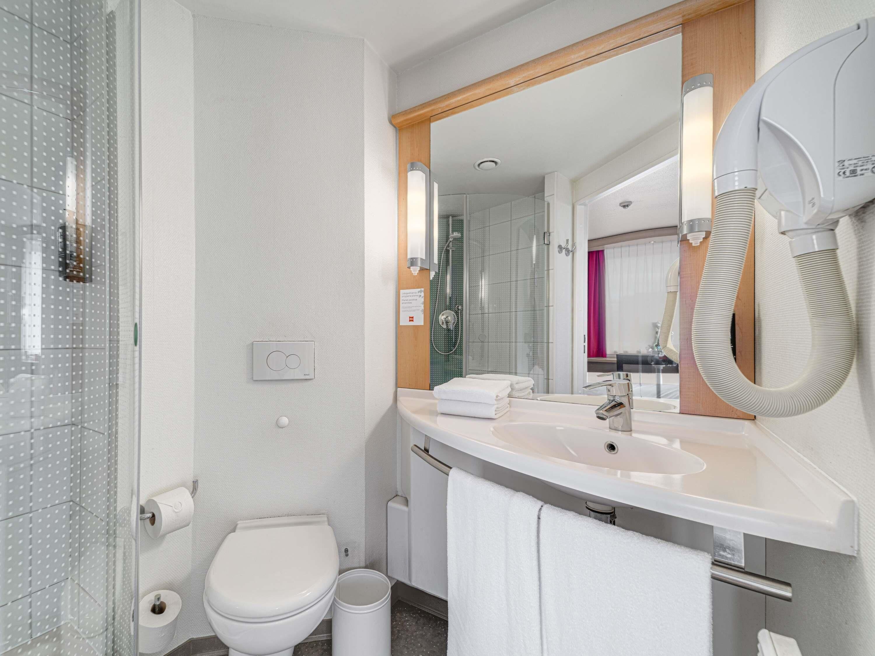 A modern bathroom with a glass shower enclosure, a white toilet, a sink with a mirror, and a towel rack.