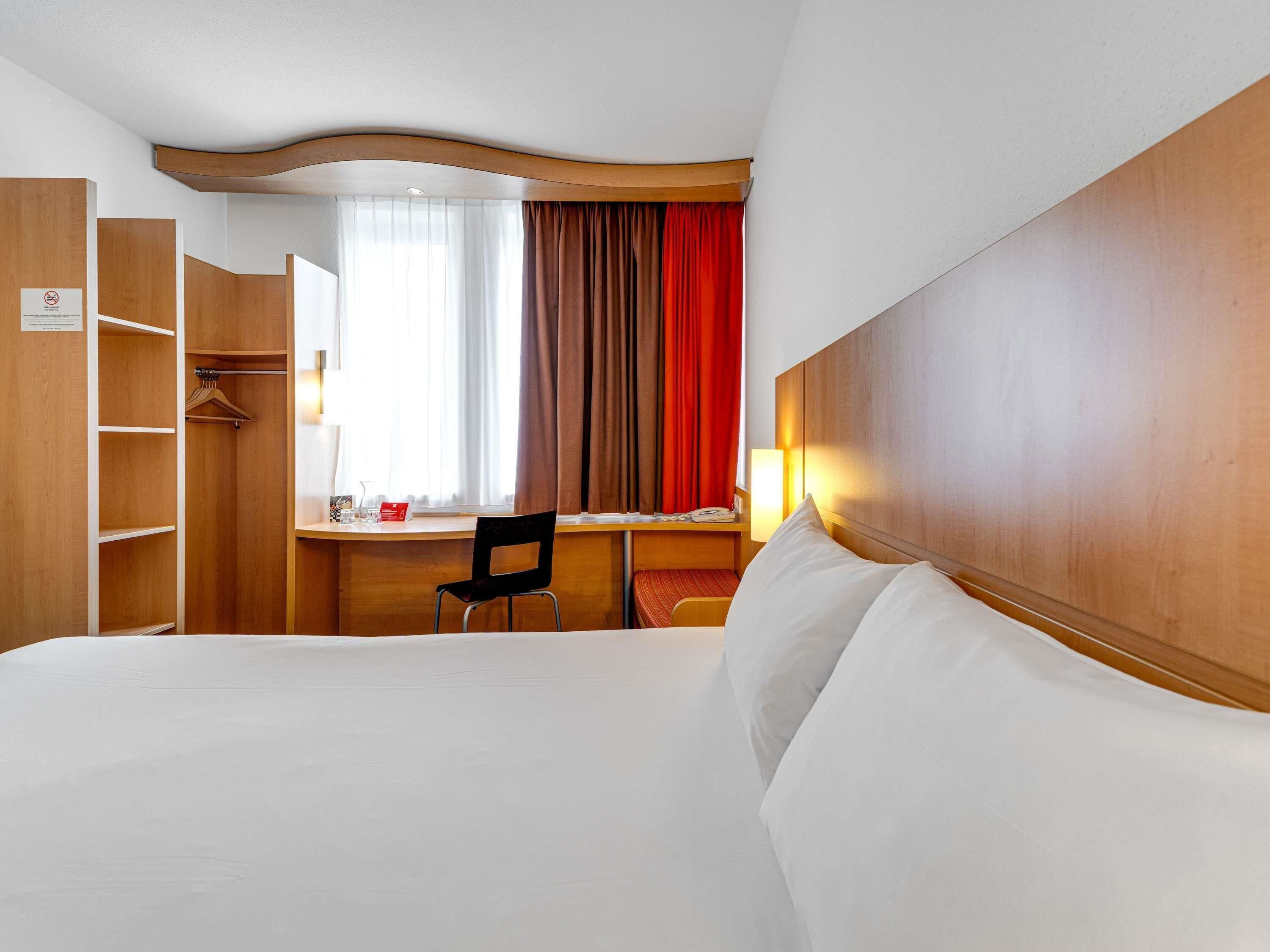 A hotel room with a bed, a desk, a chair, a wardrobe, and a window with curtains.