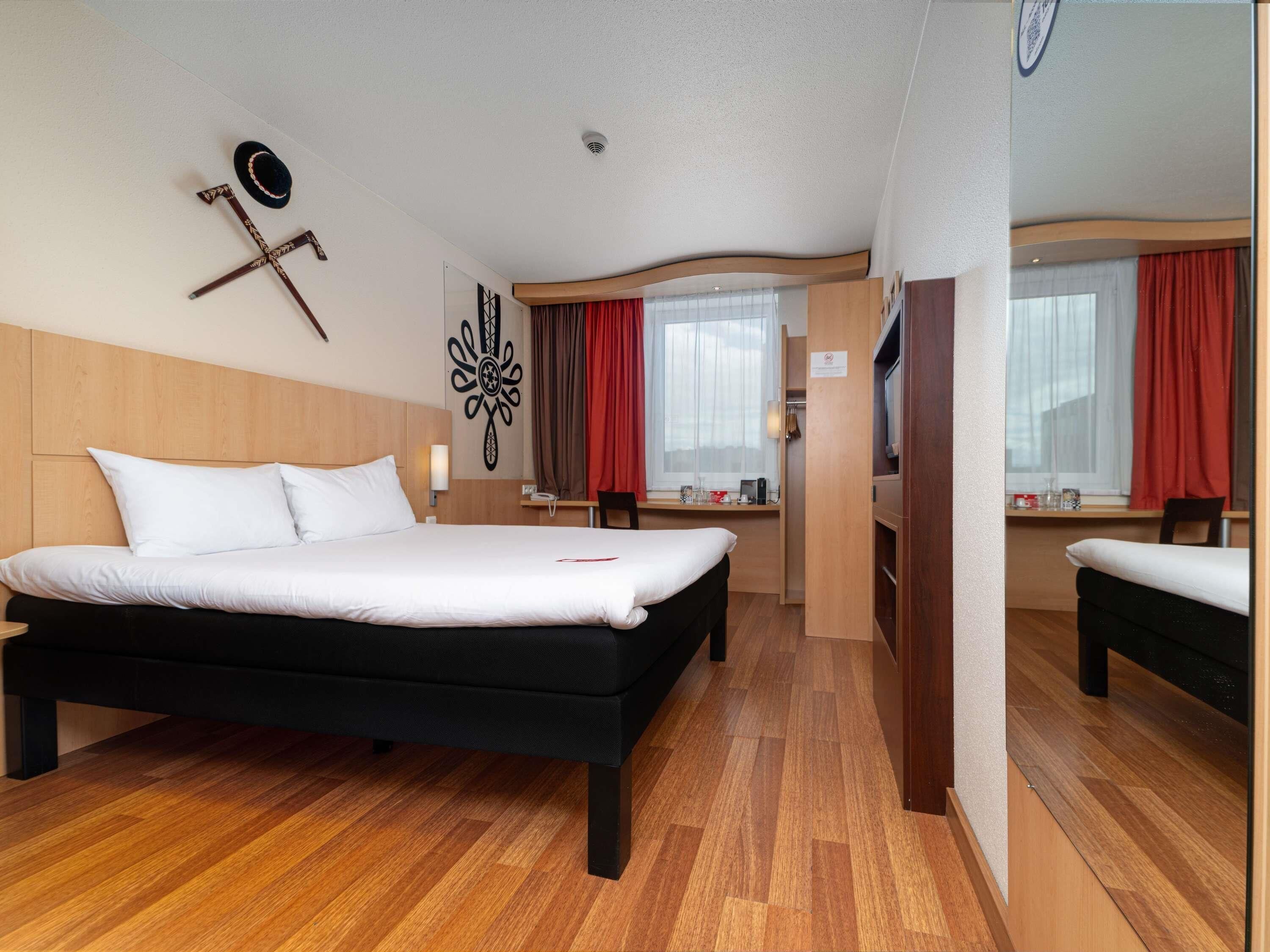 Habitación de hotel con una cama grande, un escritorio, una silla y una ventana con cortinas.