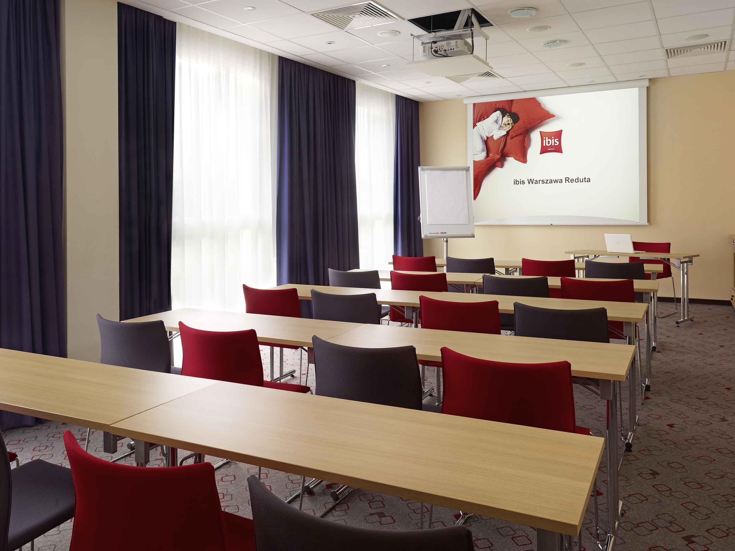 A conference room with tables and chairs, a projector screen, and a whiteboard.