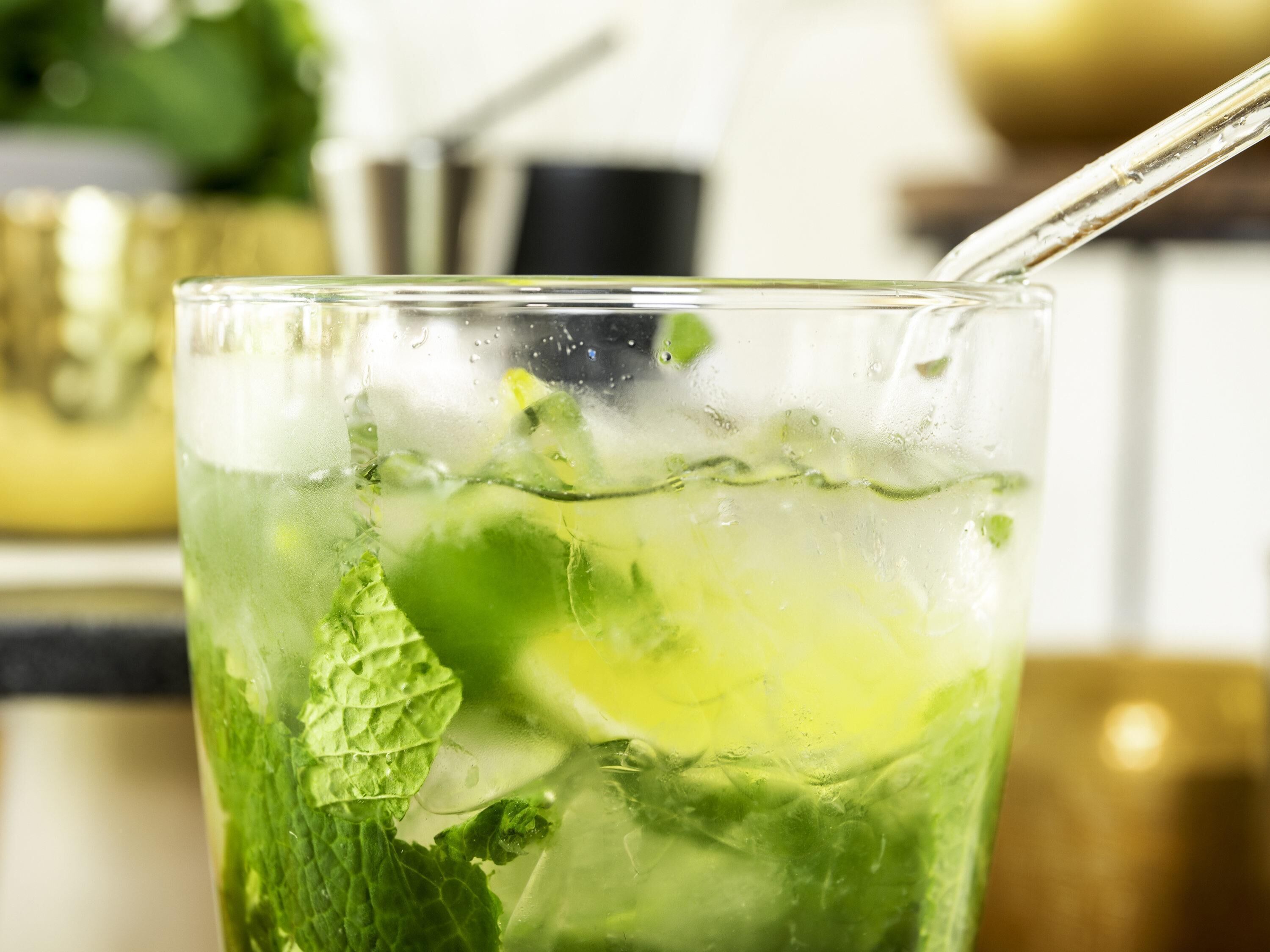 Un verre avec une paille, contenant une boisson rafraîchissante à base de glace et de feuilles de menthe.