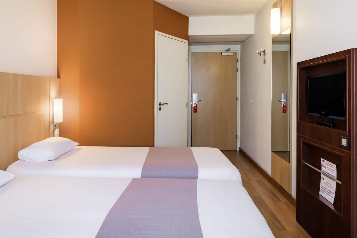 A hotel room with a bed, a TV, a mirror, and a door.