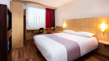 A hotel room with a large bed, a desk with a chair, a wardrobe, and a TV.