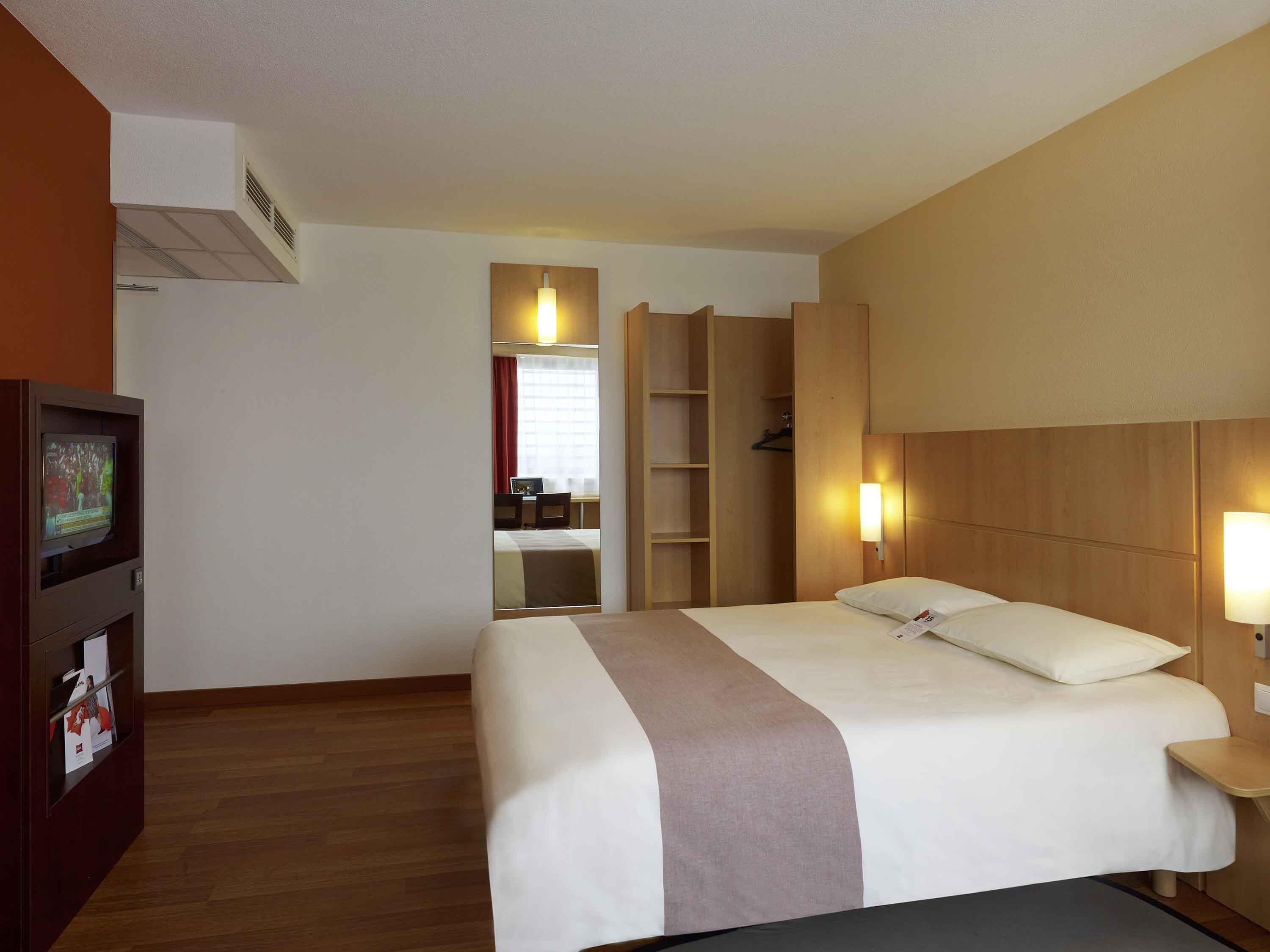 A hotel room with a bed, a TV, a desk, and a wardrobe.