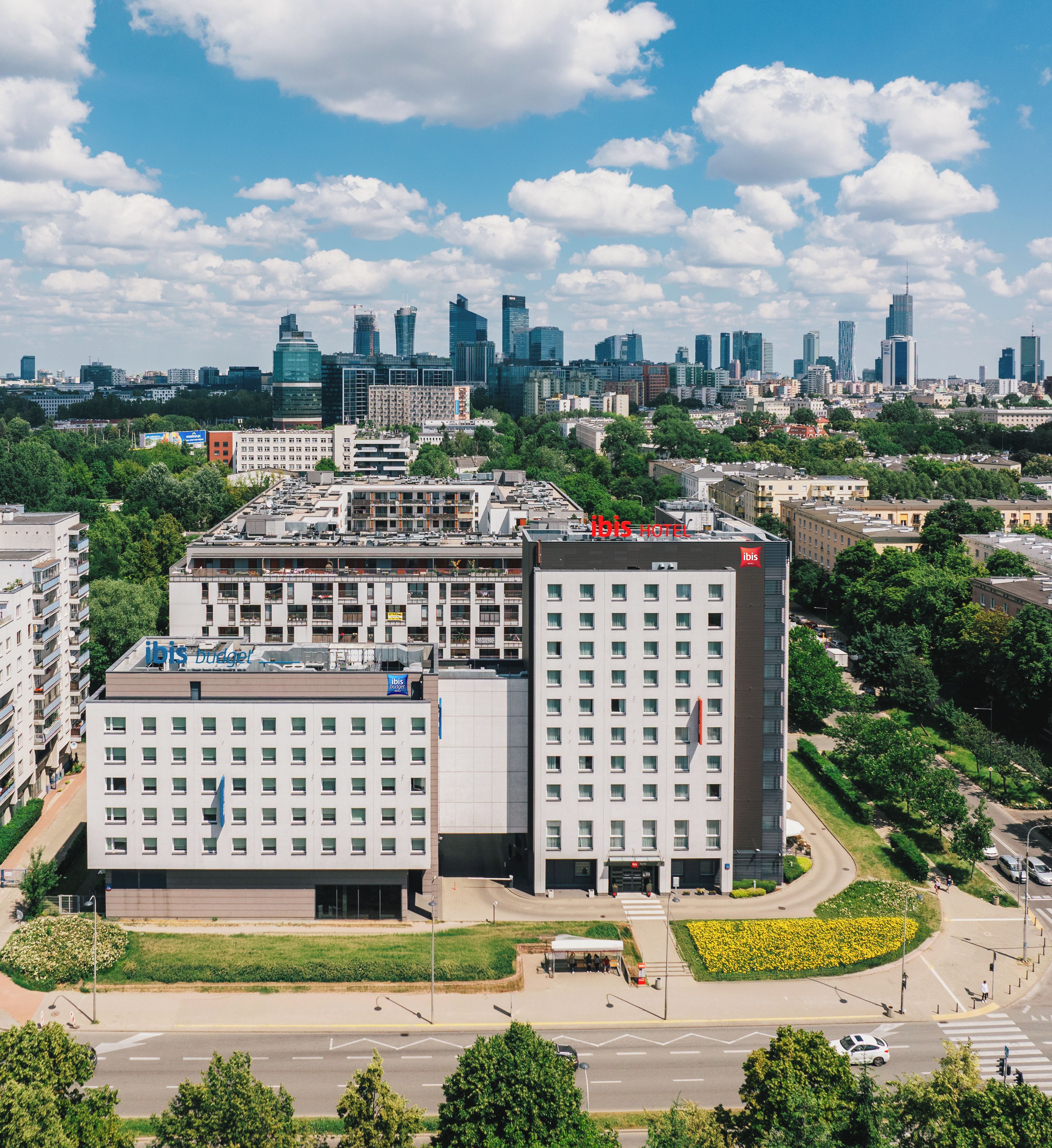 A modern hotel with a flat roof, multiple floors, and a central courtyard with a flower bed.