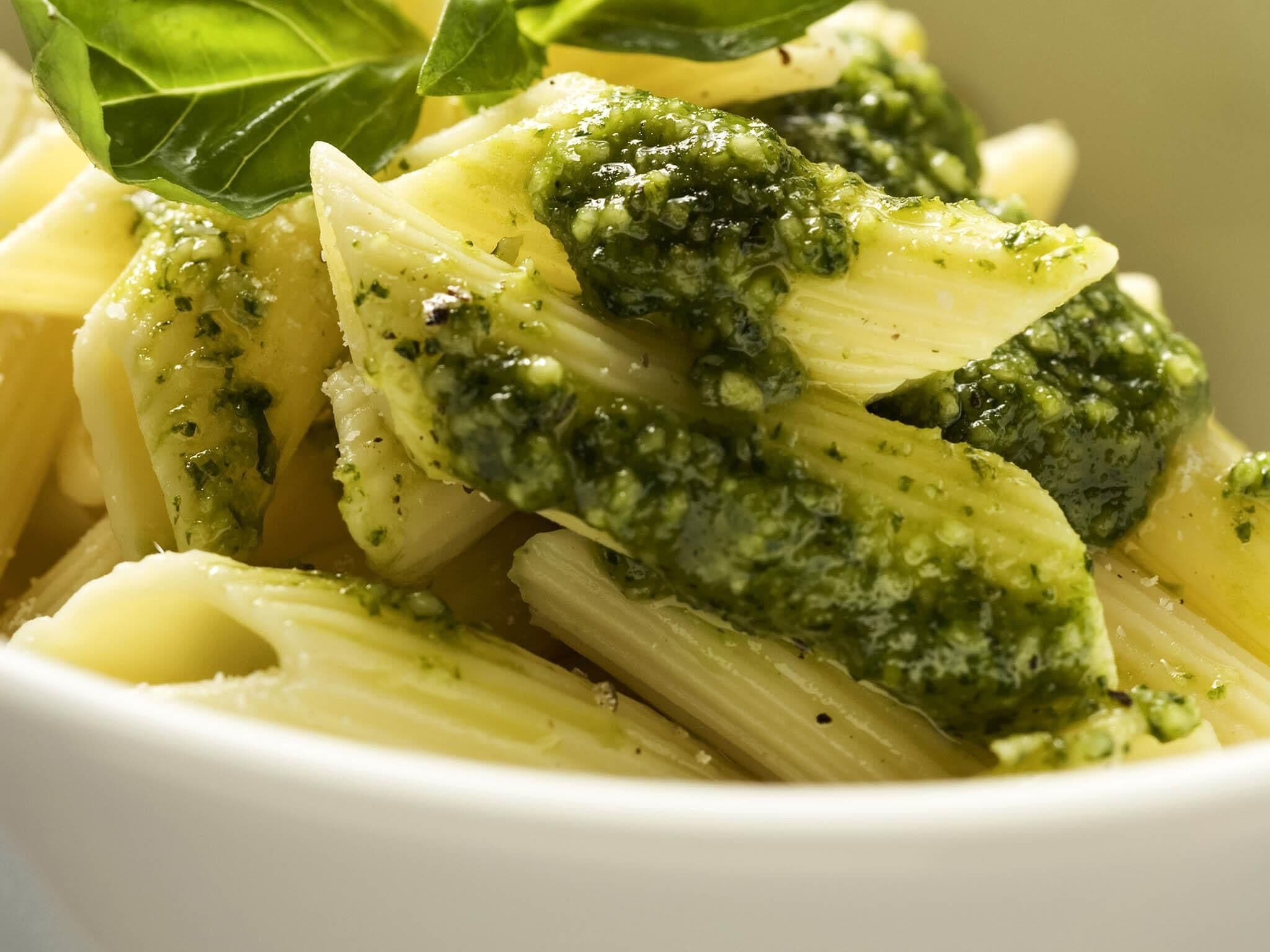 Un plat de pâtes nappées de sauce au pesto et garni de feuilles de basilic.