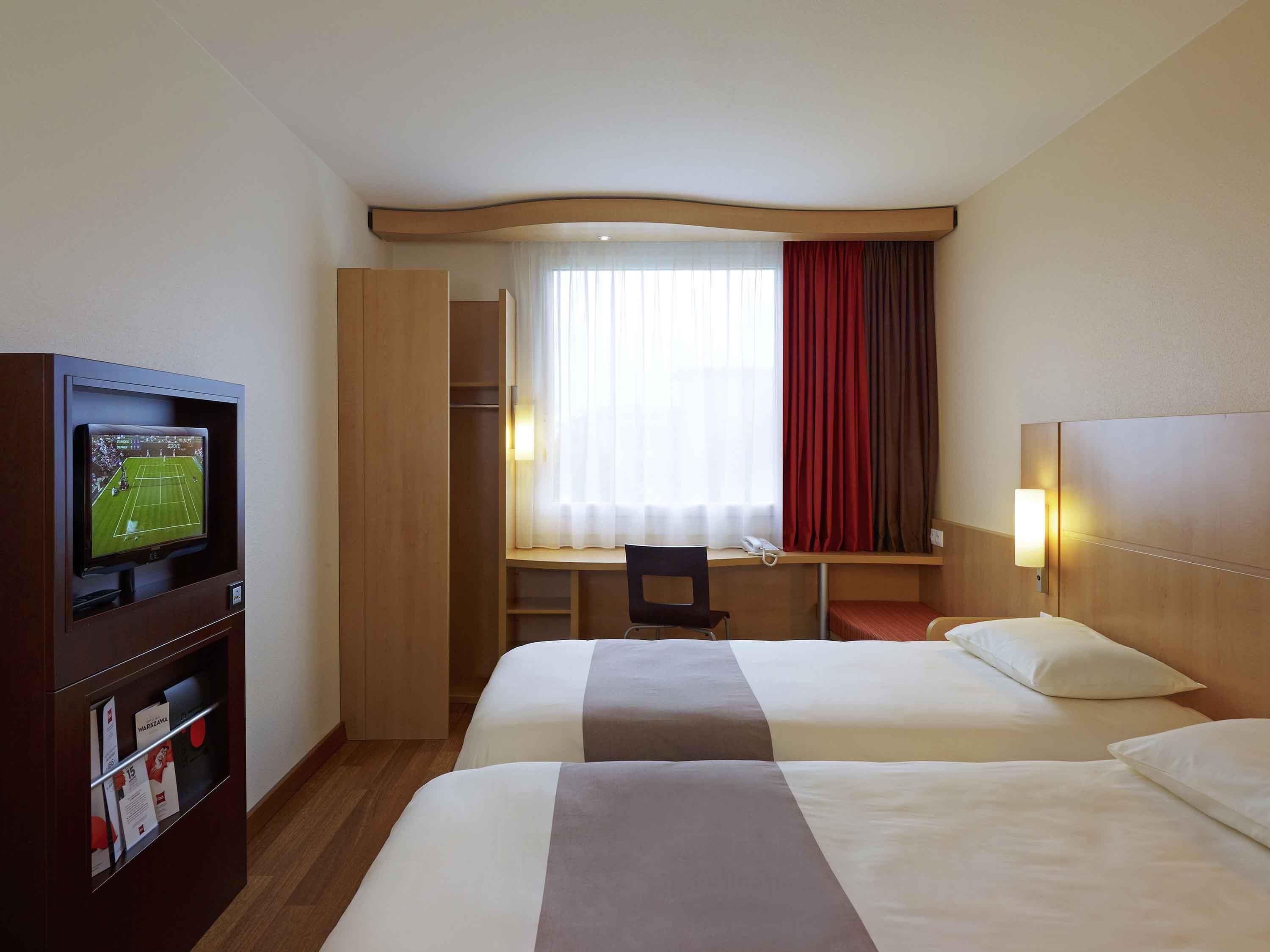 Ein Hotelzimmer mit zwei Betten, einem Schreibtisch, einem Fernseher und einem Kleiderschrank.